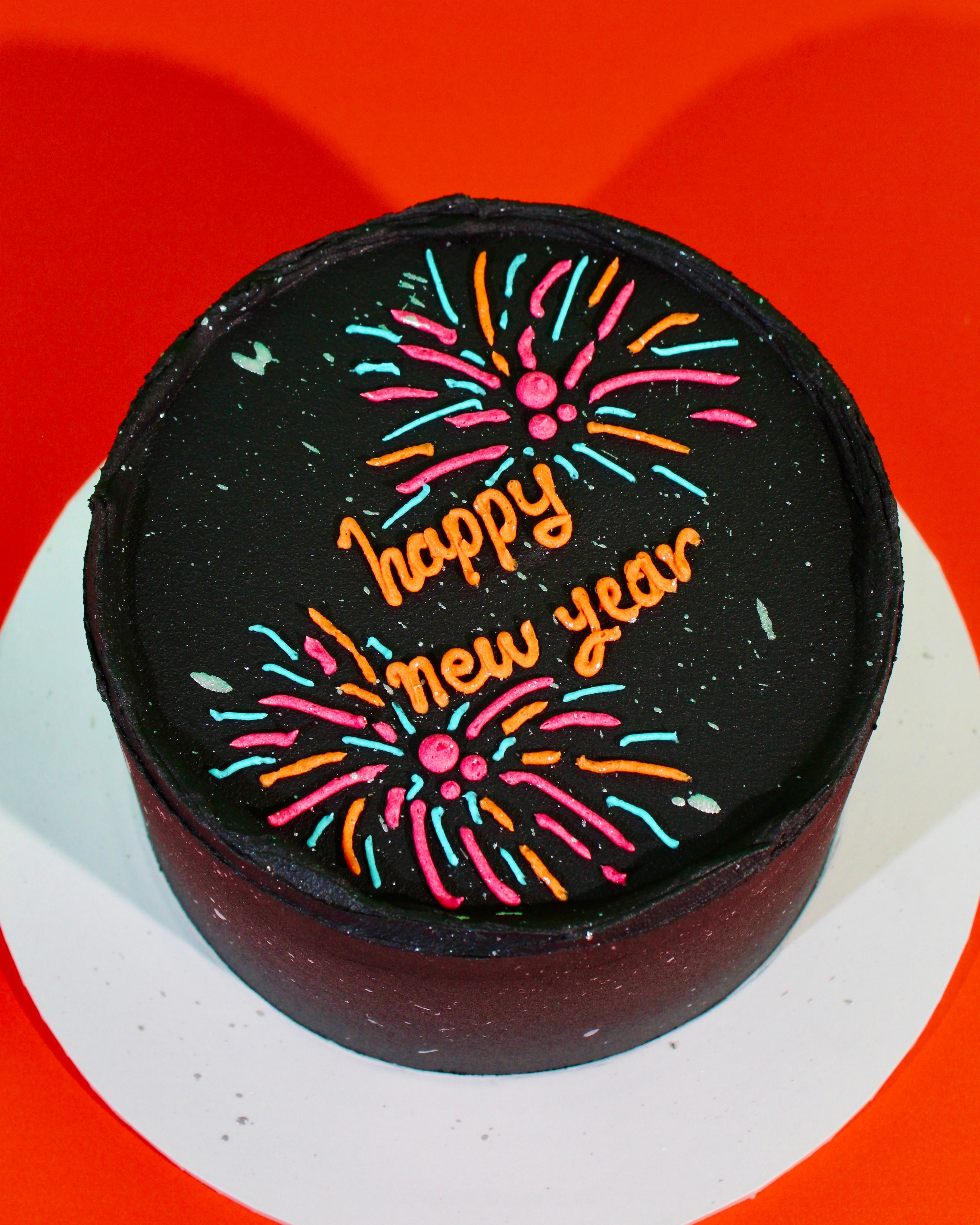 Black New Year’s cake with neon piped fireworks and “happy new year” lettering