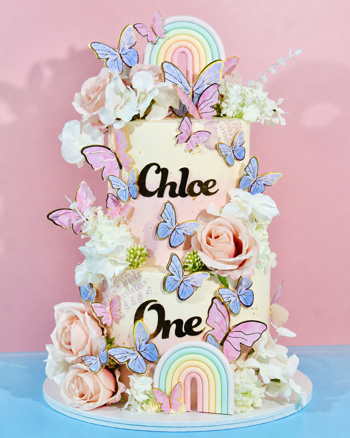 Decorative cake with flowers, butterflies, and rainbow elements on a pink background