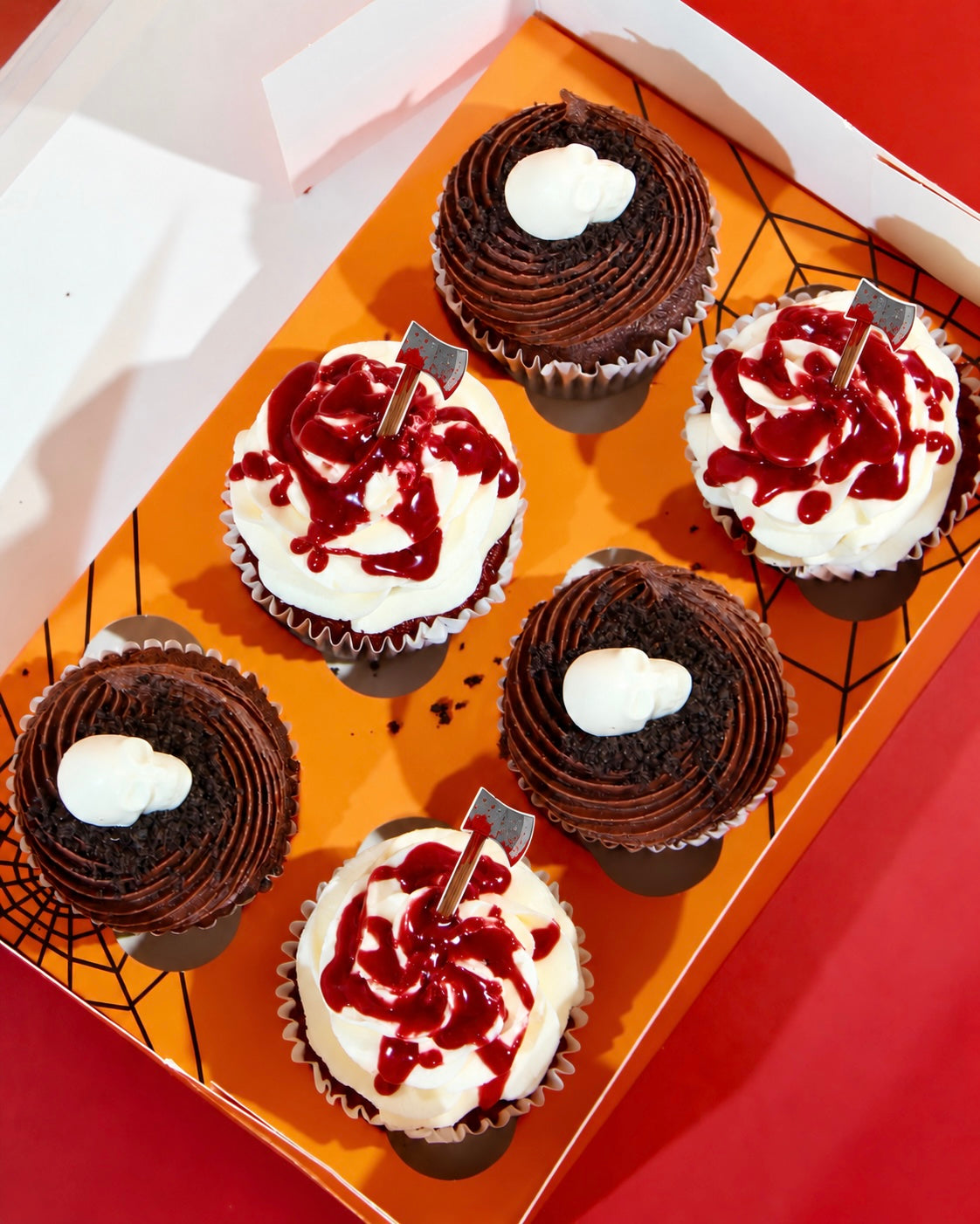 Box of six Halloween cupcakes with skull and blood splatter axe designs in orange Halloween spider web gift box