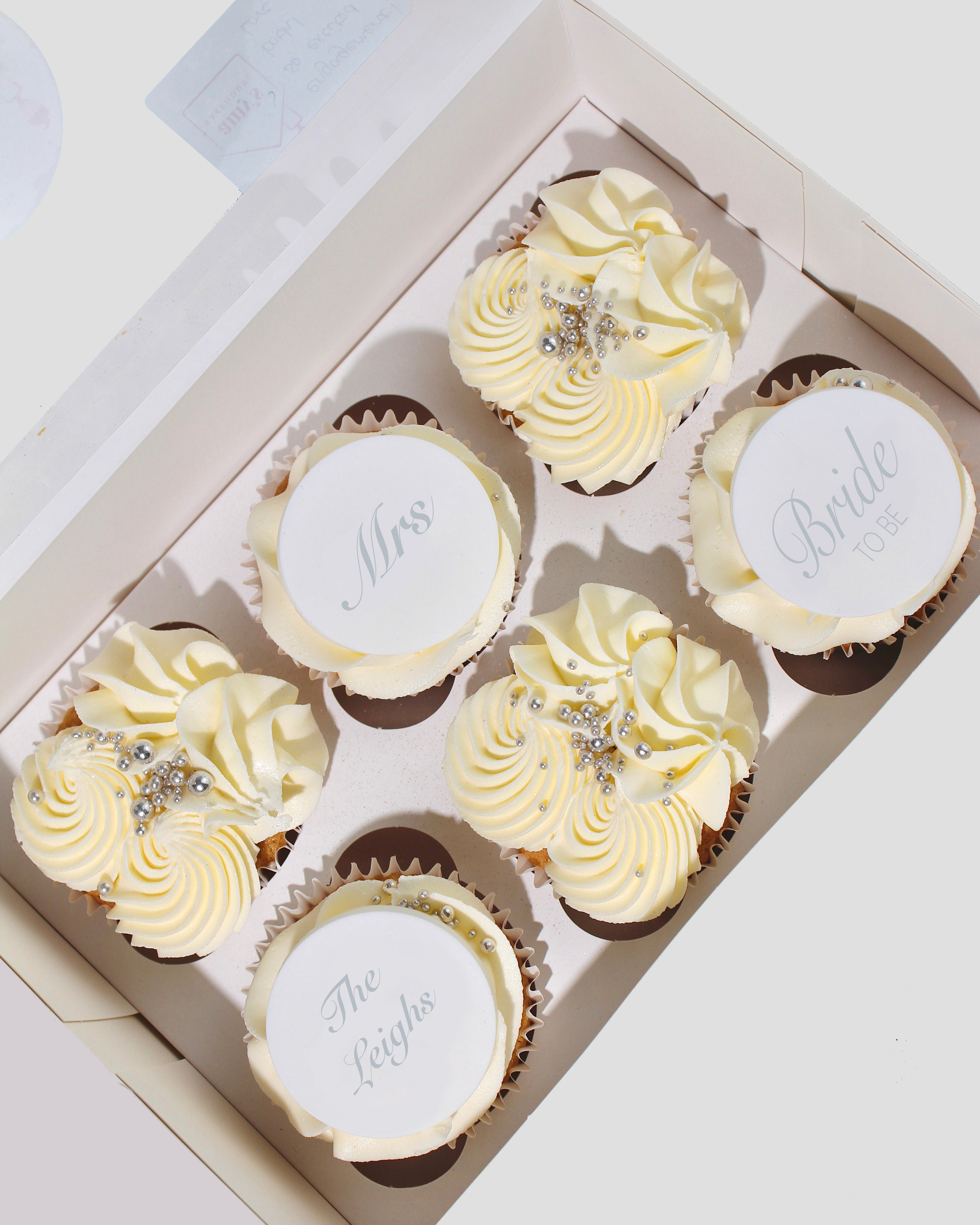 Box of elegant bridal cupcakes decorated with pearls and custom toppers.