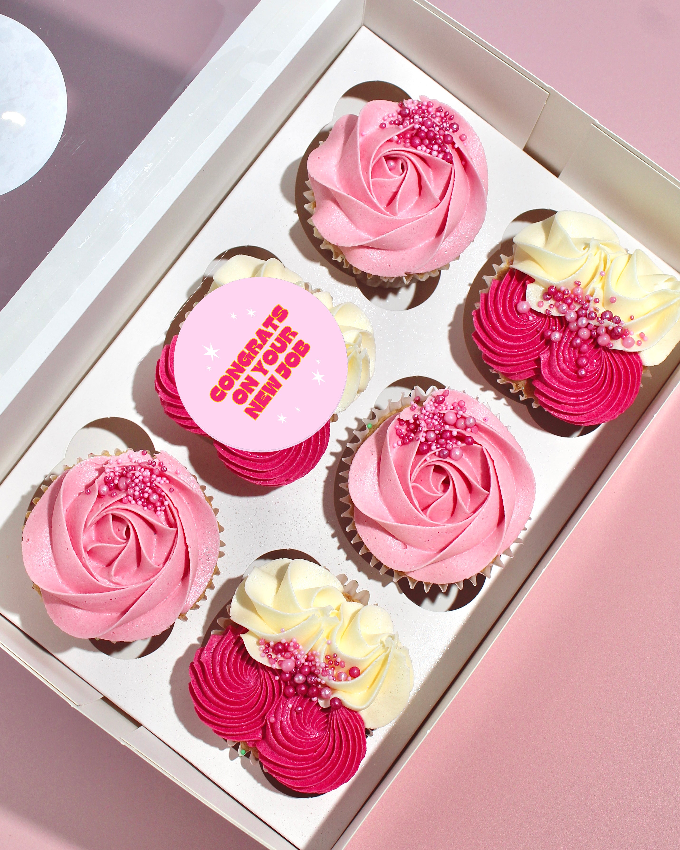 Box of pink New Job cupcakes with piped buttercream, sprinkles and personalised topper option.