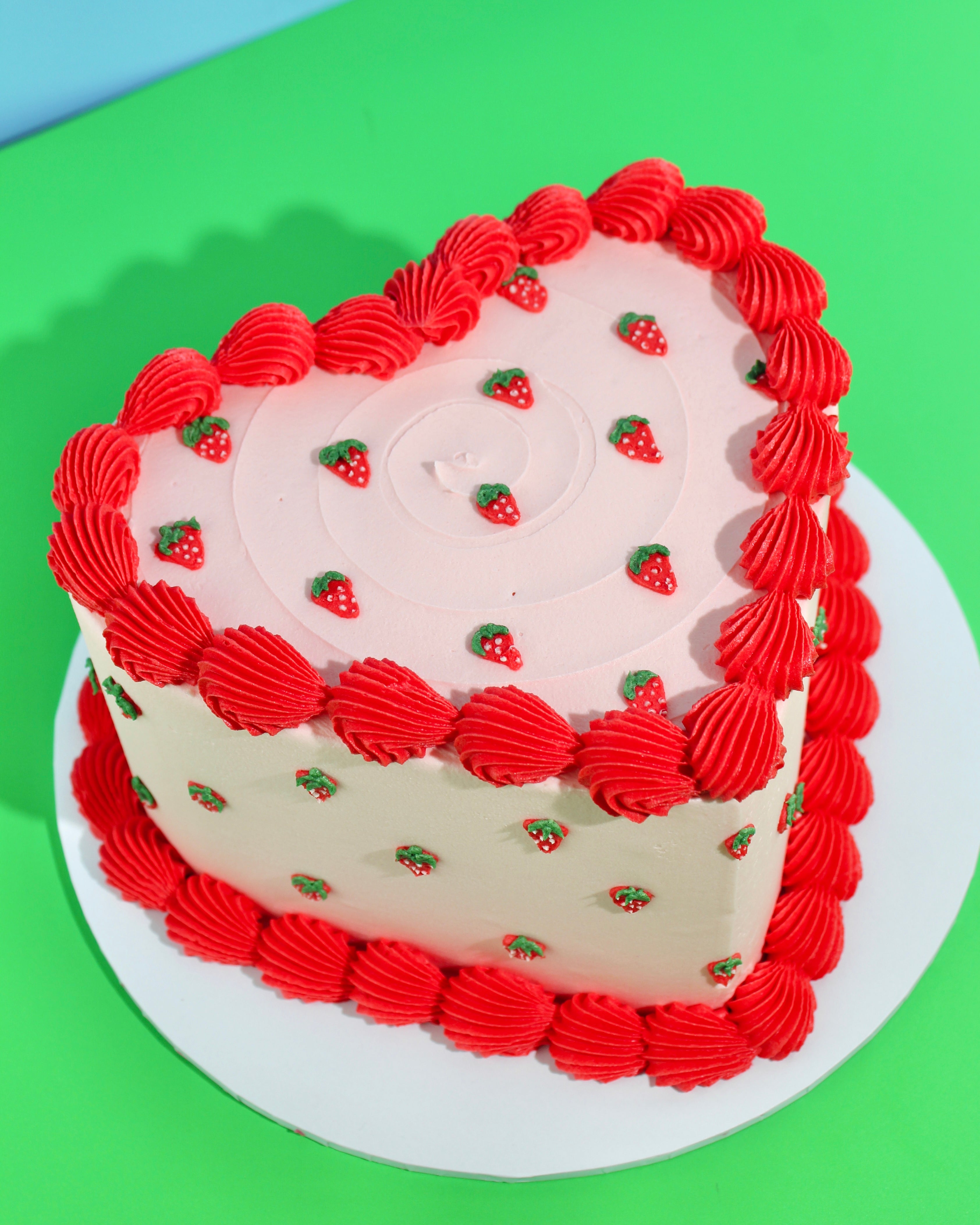 Strawberry-themed cake with pink buttercream, piped strawberries and red buttercream piping