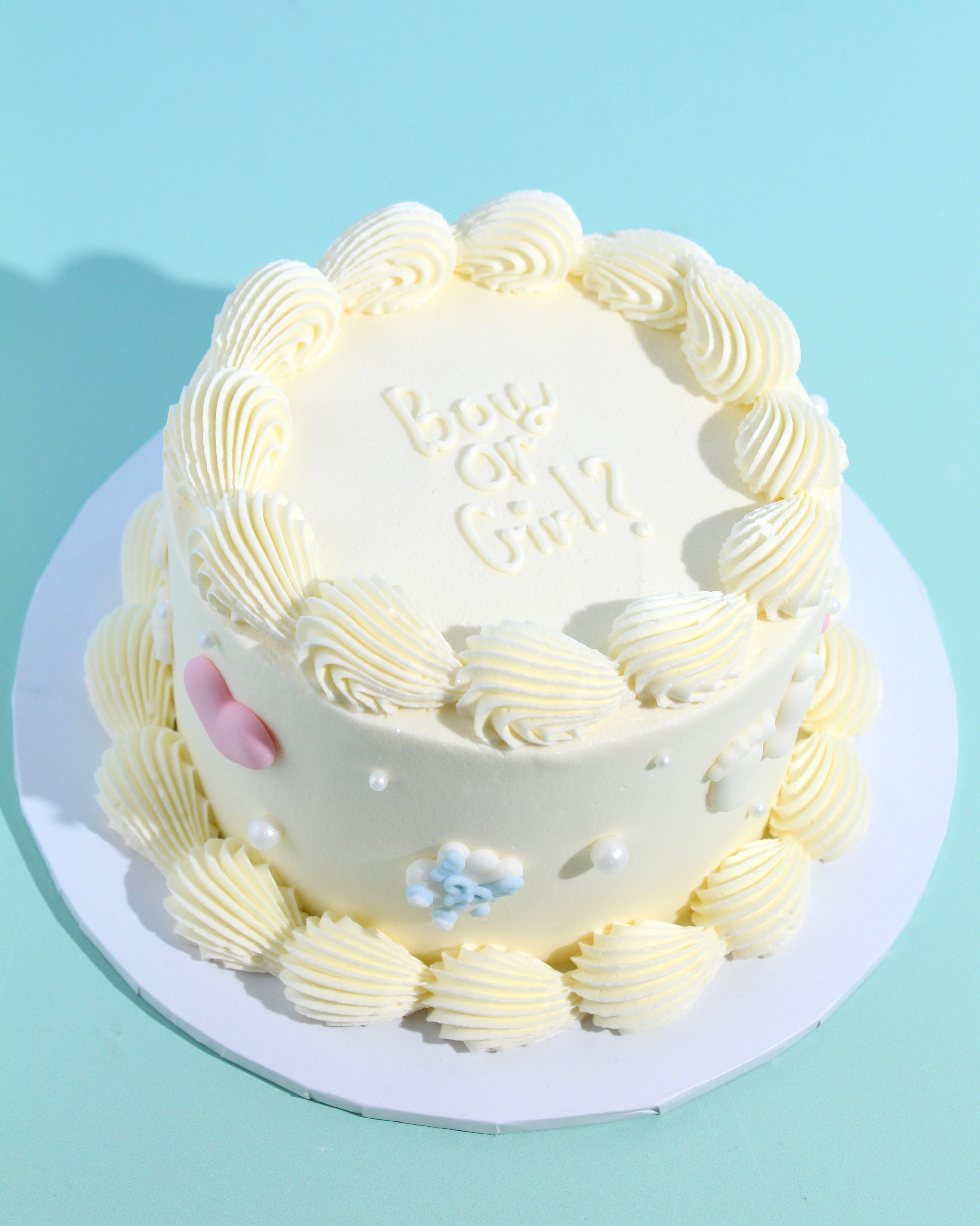 Mini gender reveal cake with piped white buttercream, baby-themed decorations, and “Boy or Girl?” message on top.