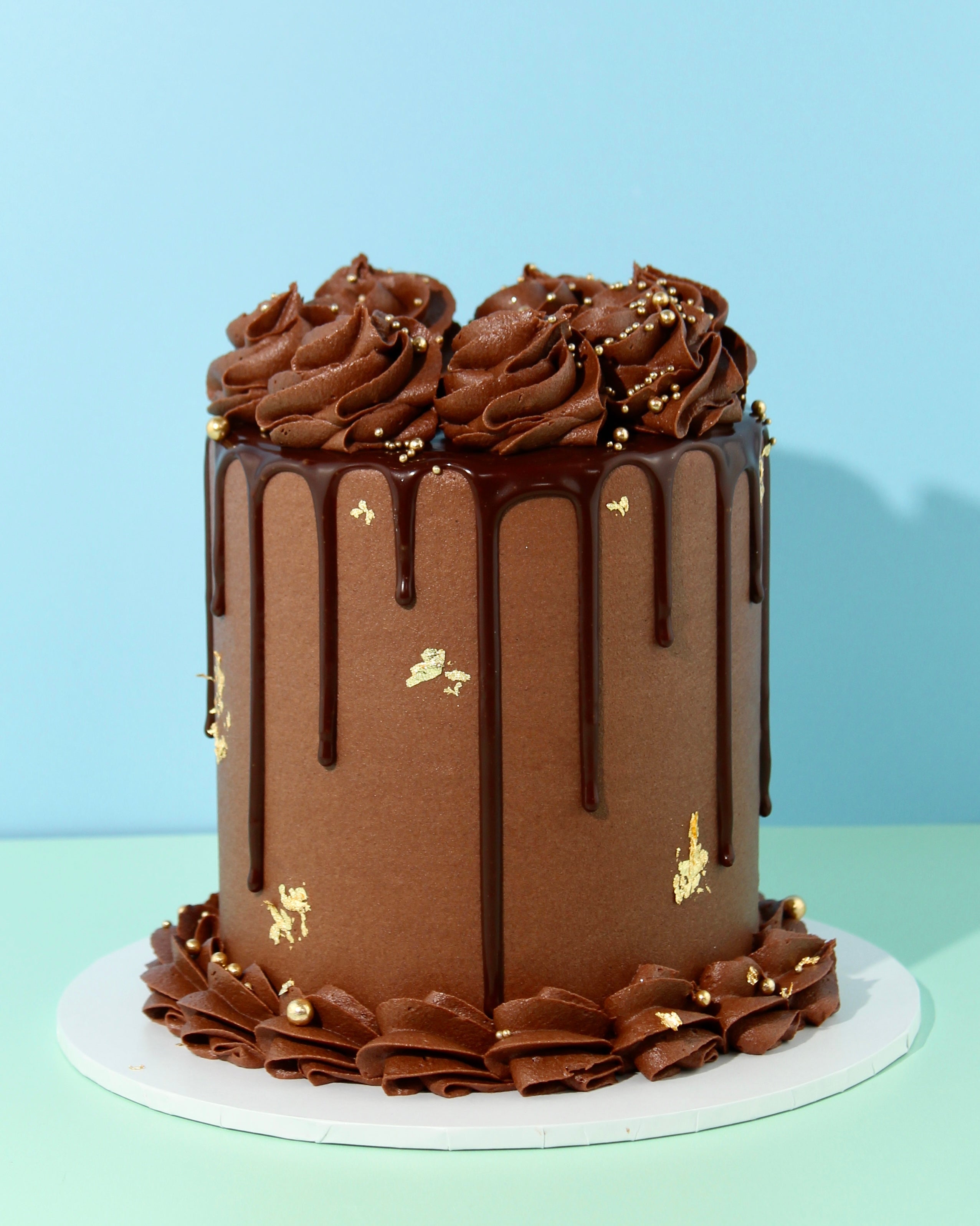 Tall triple chocolate cake with chocolate drip, piped swirls and gold decorations