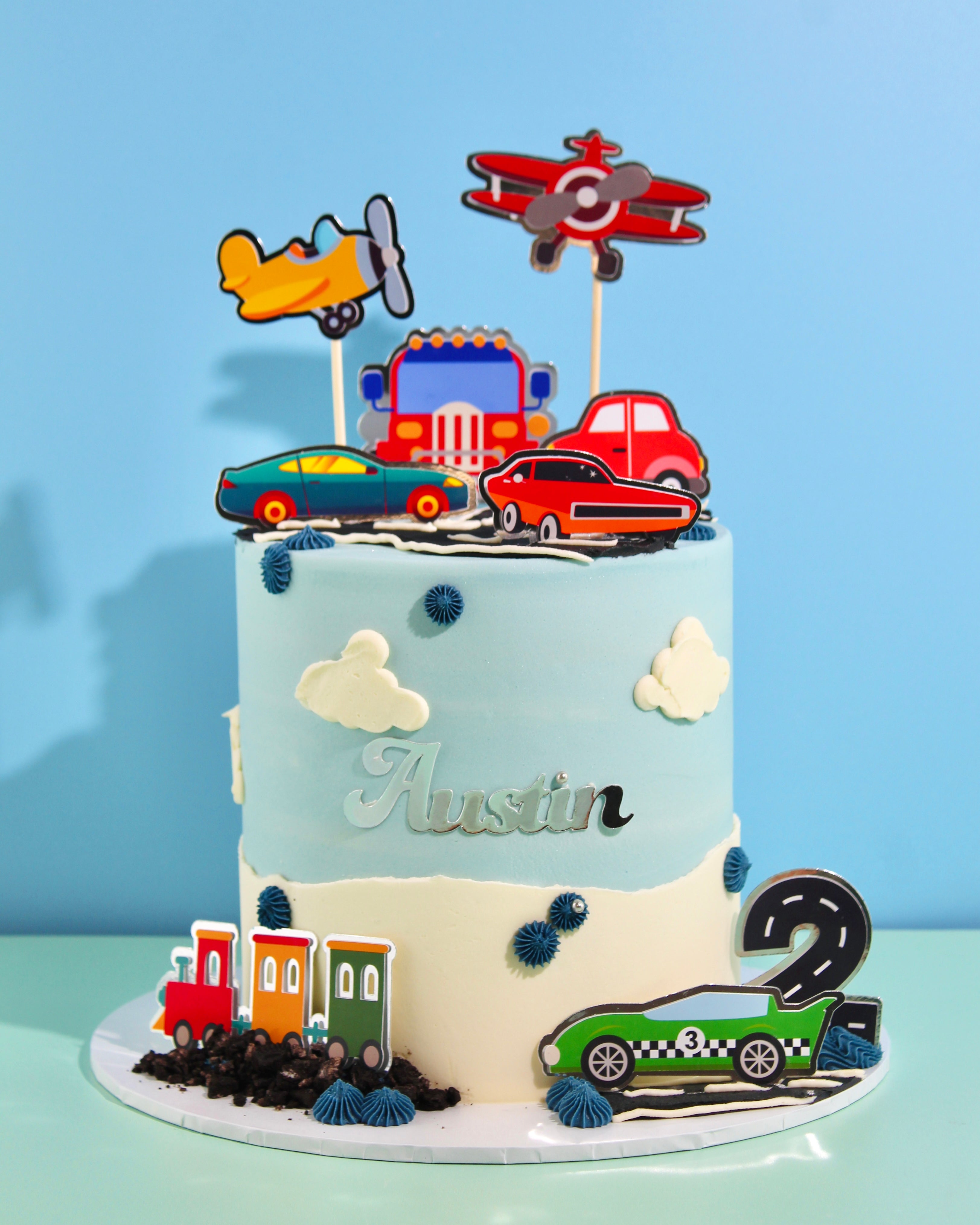 Transport-themed cake with pastel buttercream, car and plane toppers, clouds and winding road decoration