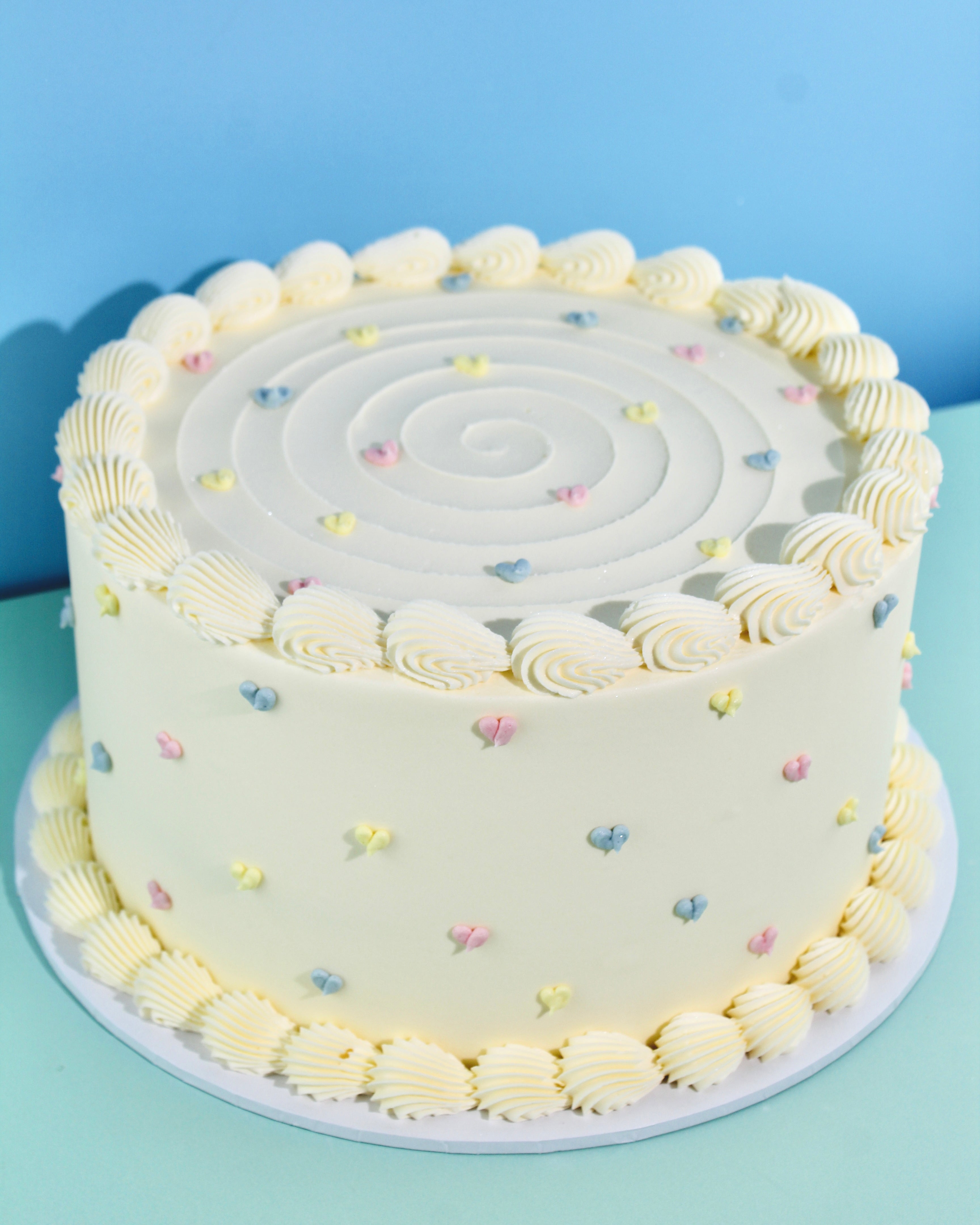Pastel buttercream cake with delicate piped hearts and swirl design on top