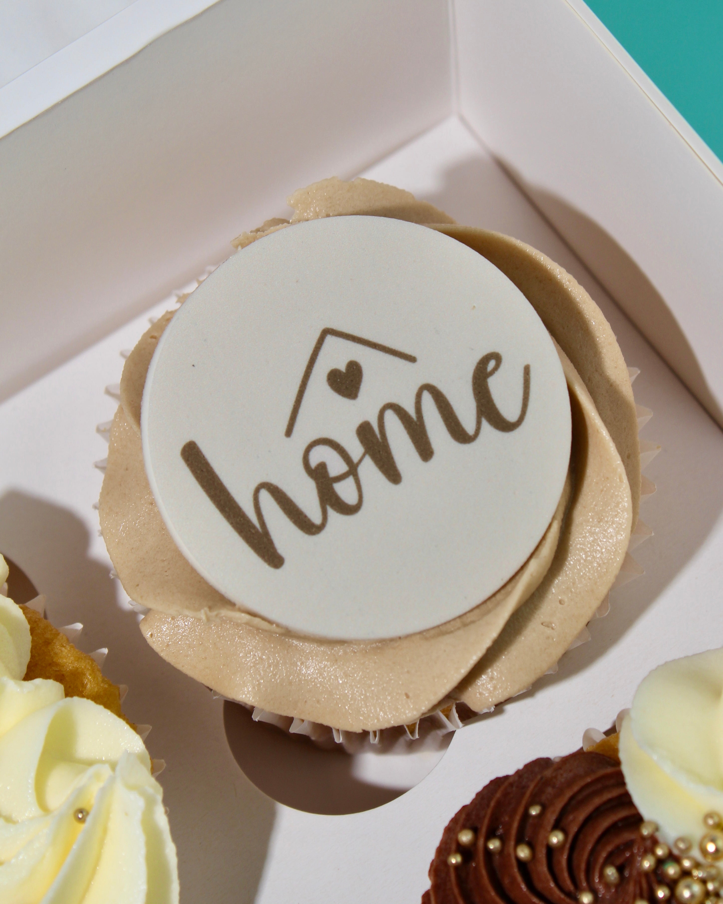 Close-up of beige buttercream cupcake with an edible “Home” topper