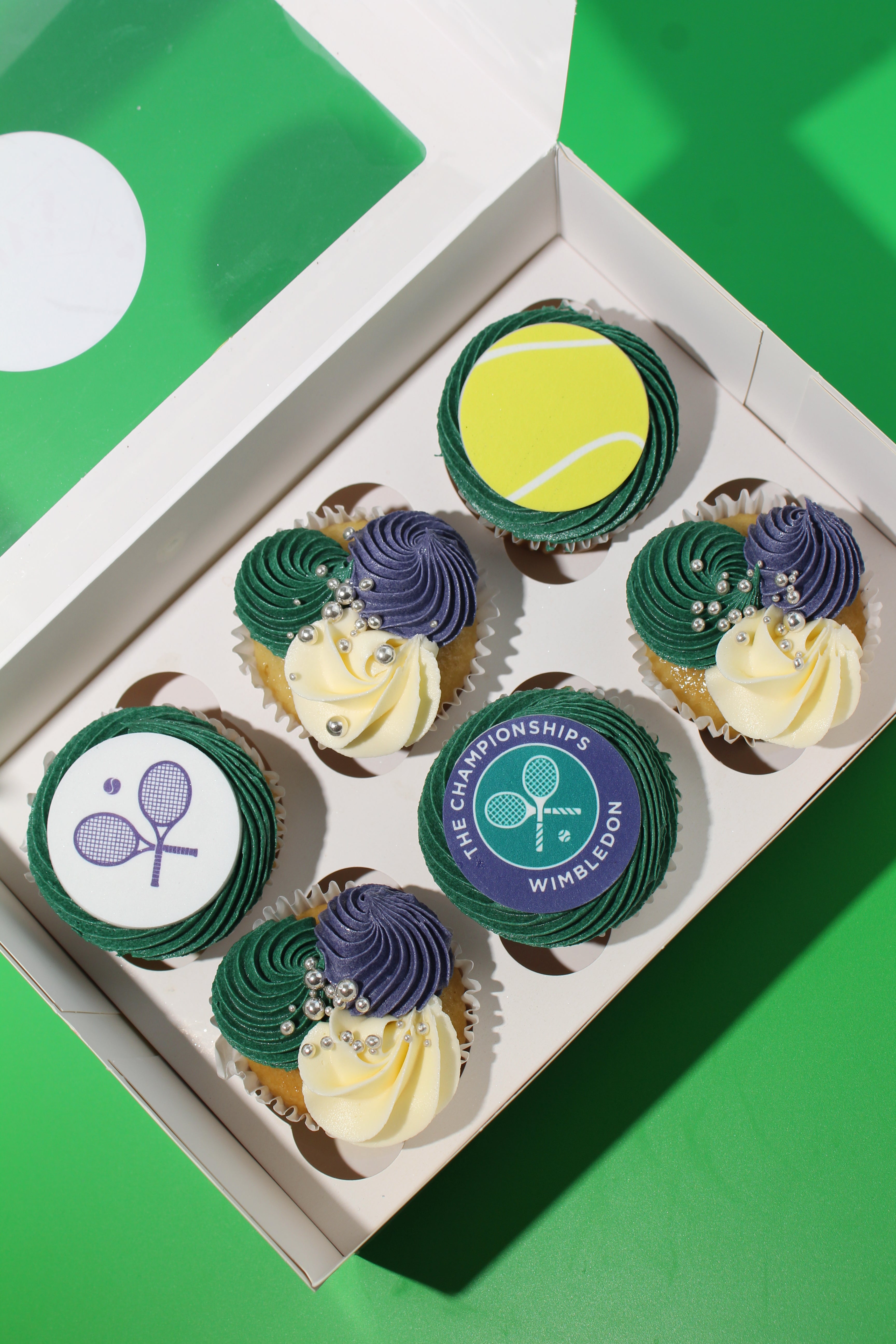 Box of six Wimbledon cupcakes with Championships logo, tennis ball and racket discs in green and purple buttercream
