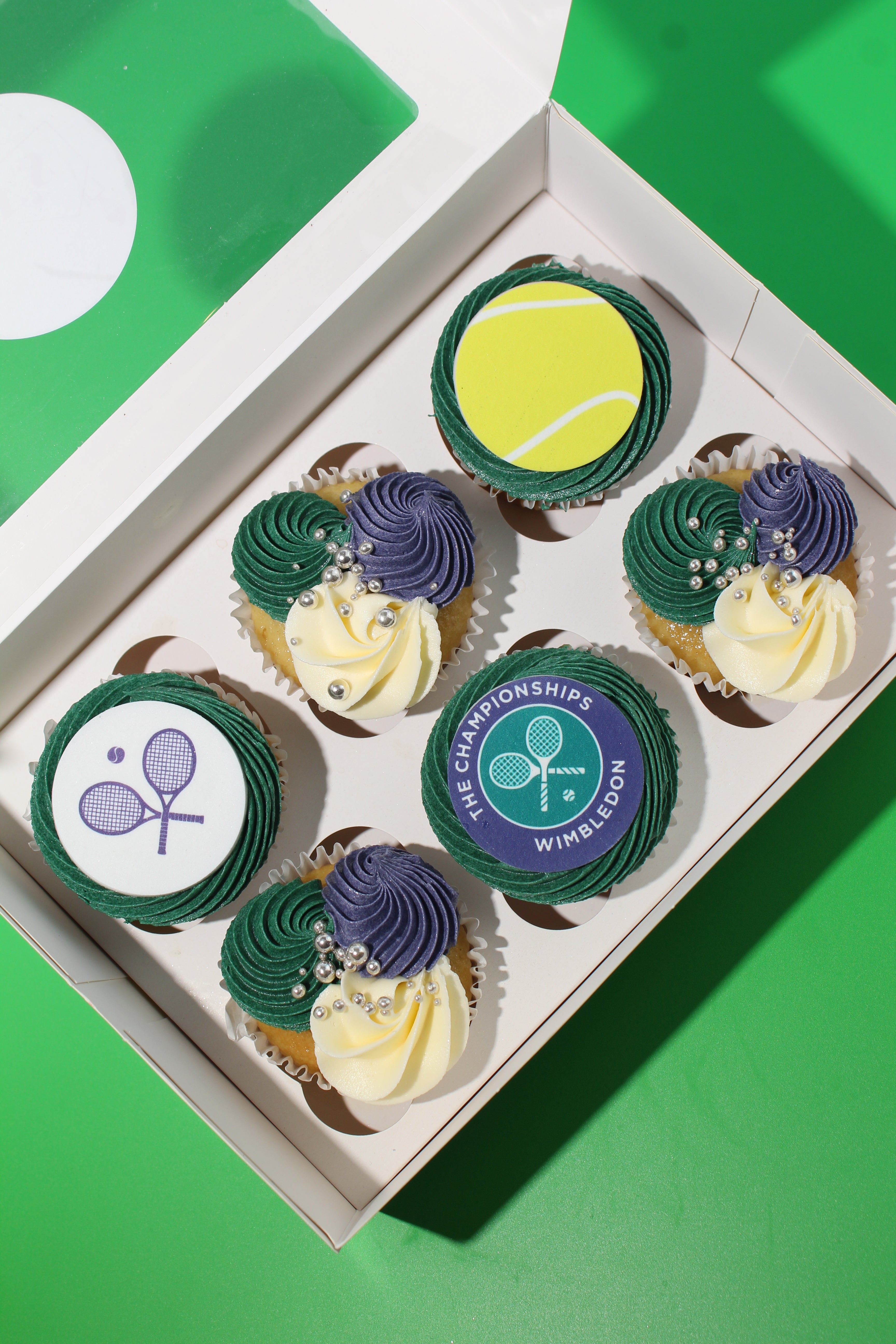 Top-down view of Wimbledon cupcake box showing Championships logo and tennis ball disc with silver pearl detail
