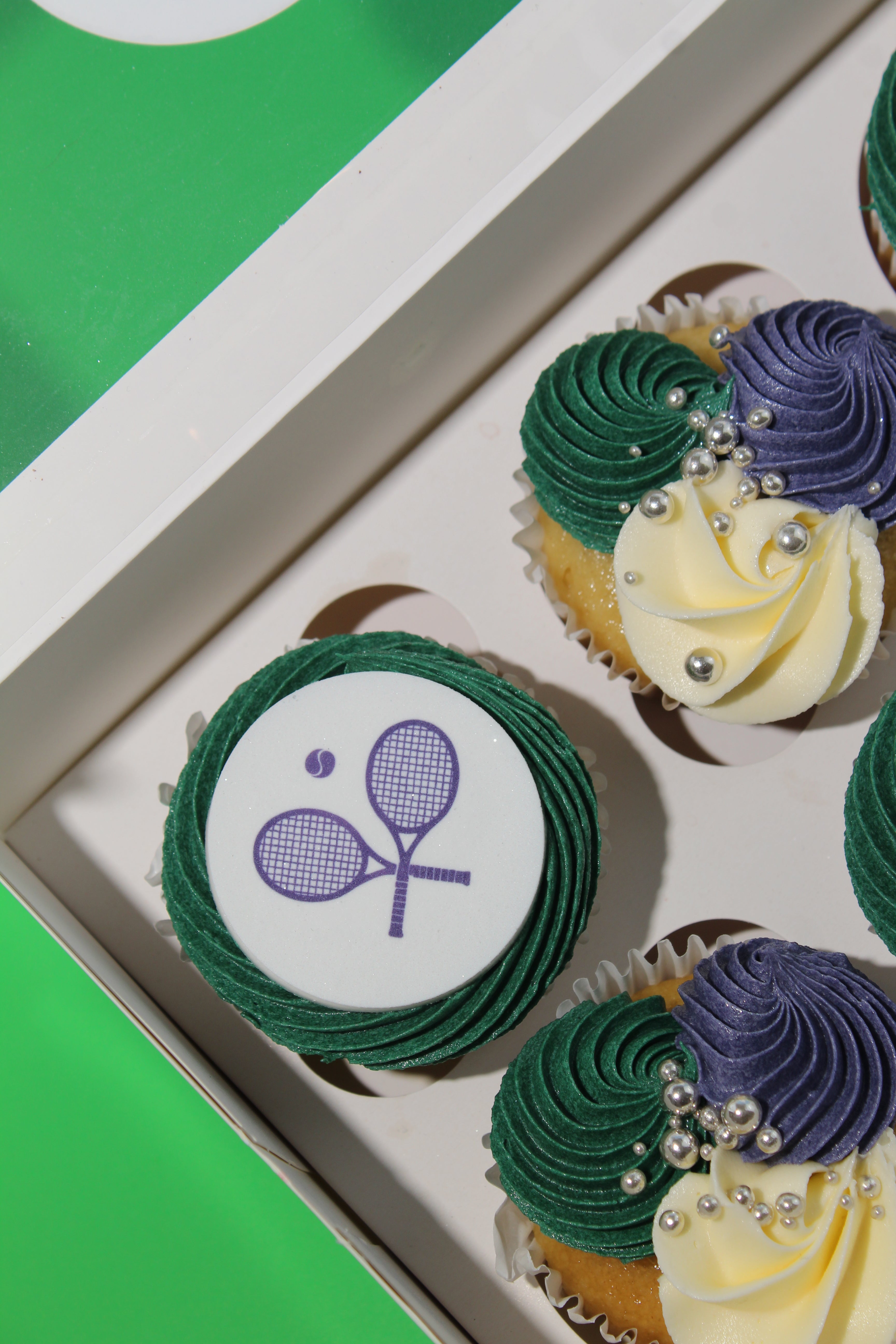 Close-up of Wimbledon cupcake with crossed tennis racket disc and green purple swirled buttercream rosette
