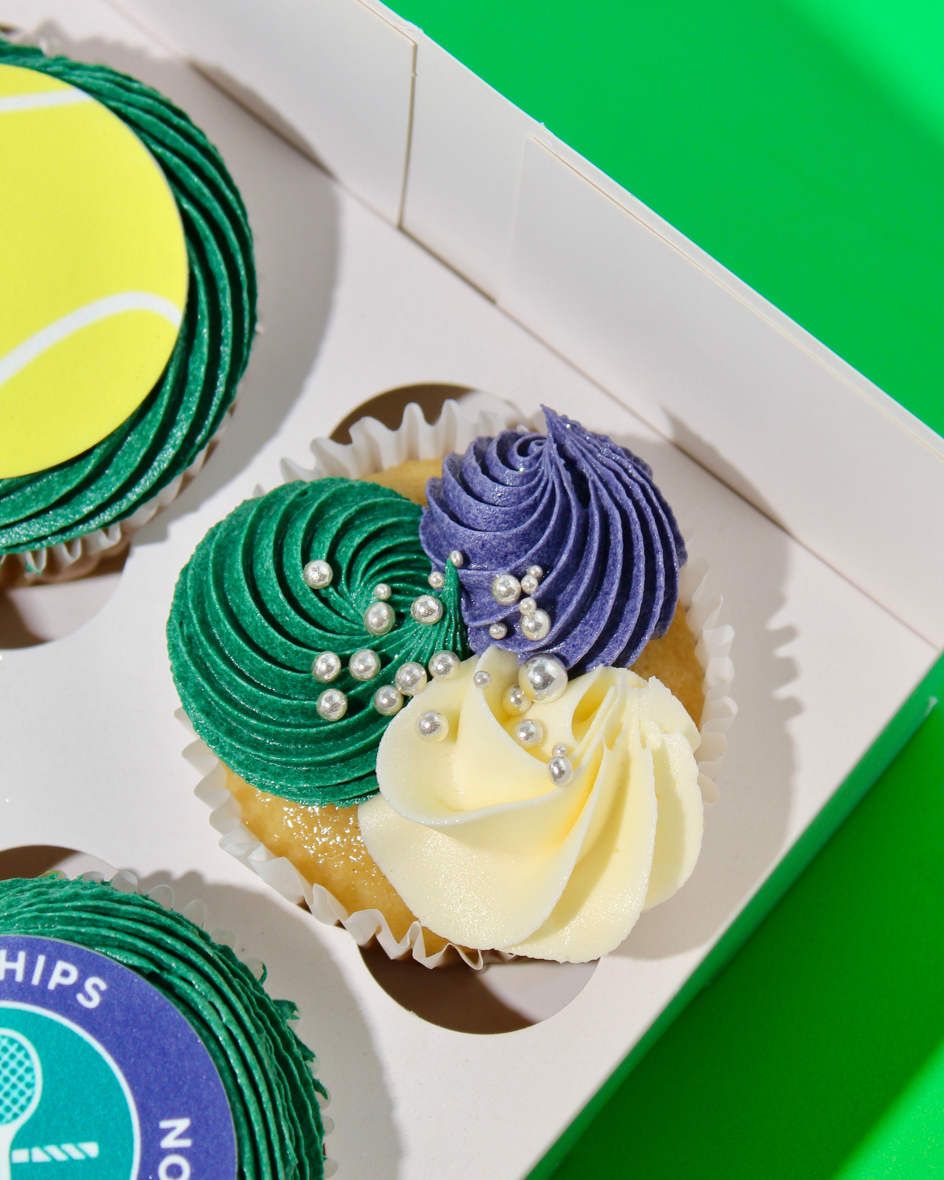 Close-up of Wimbledon cupcake showing three-tone green purple and cream buttercream swirls with silver pearls


