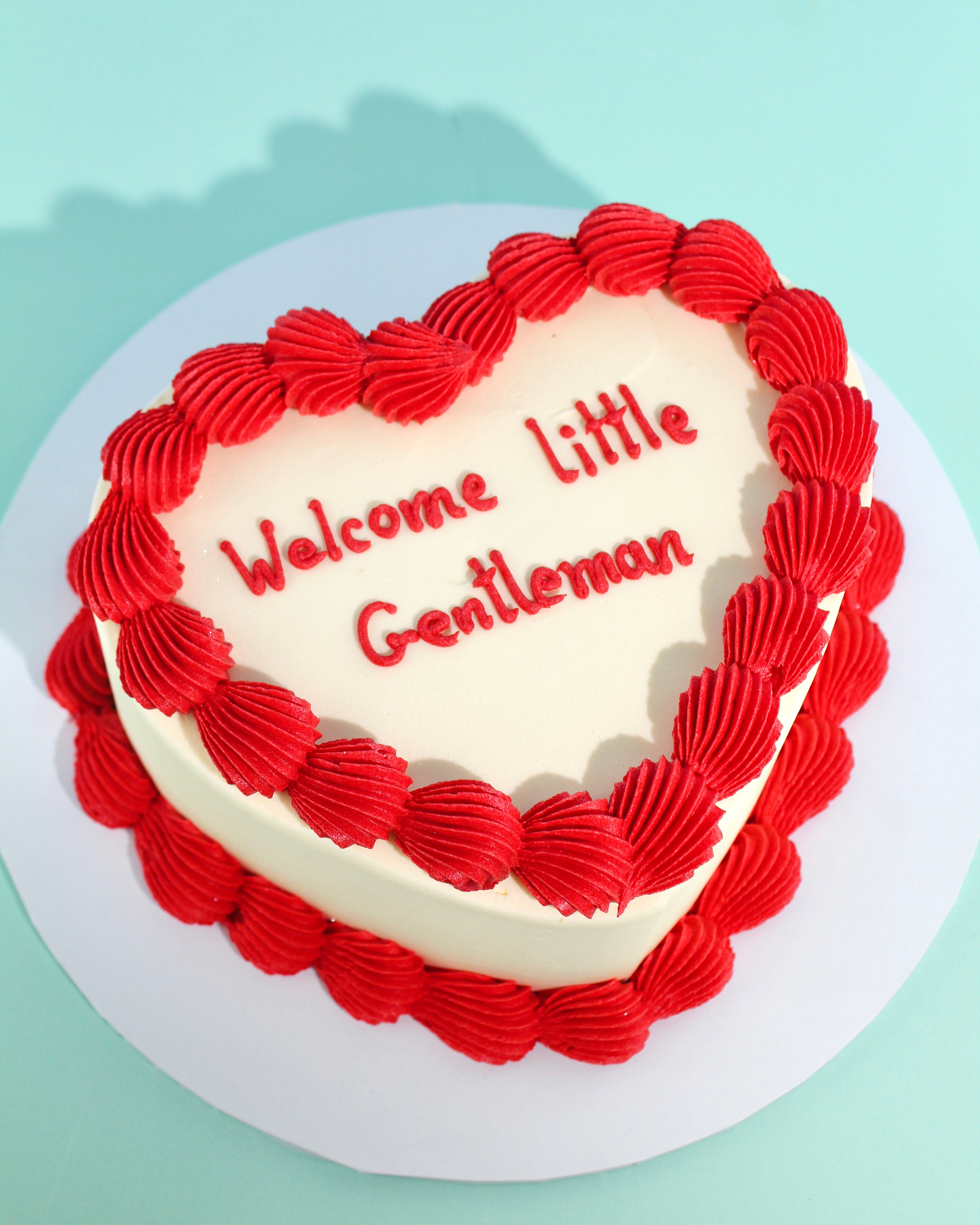 Mini heart-shaped cake with red piped buttercream border and custom message on top