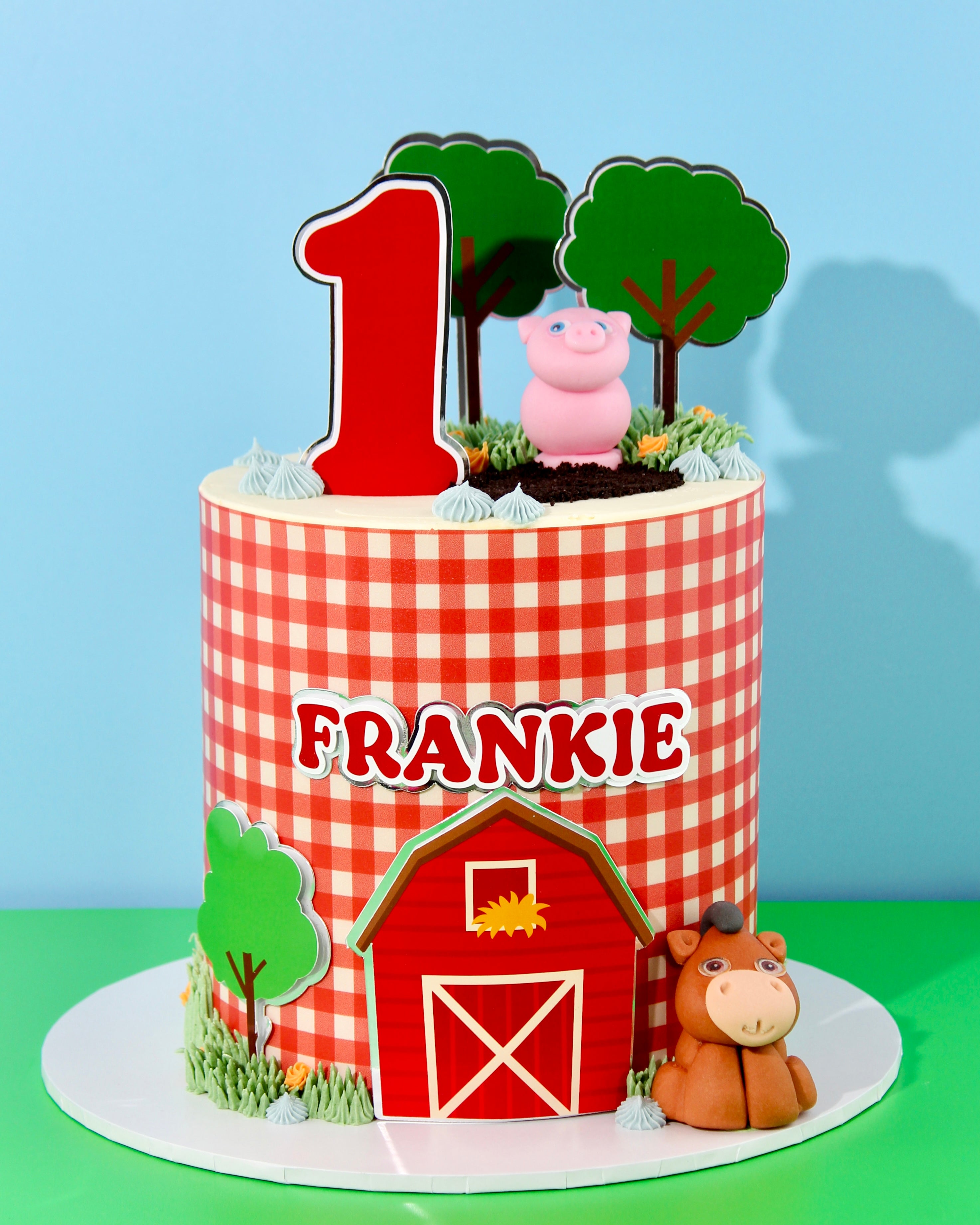 Children's birthday cake with farm theme, number 1, pig, horse, and checkered pattern on a blue and green background.