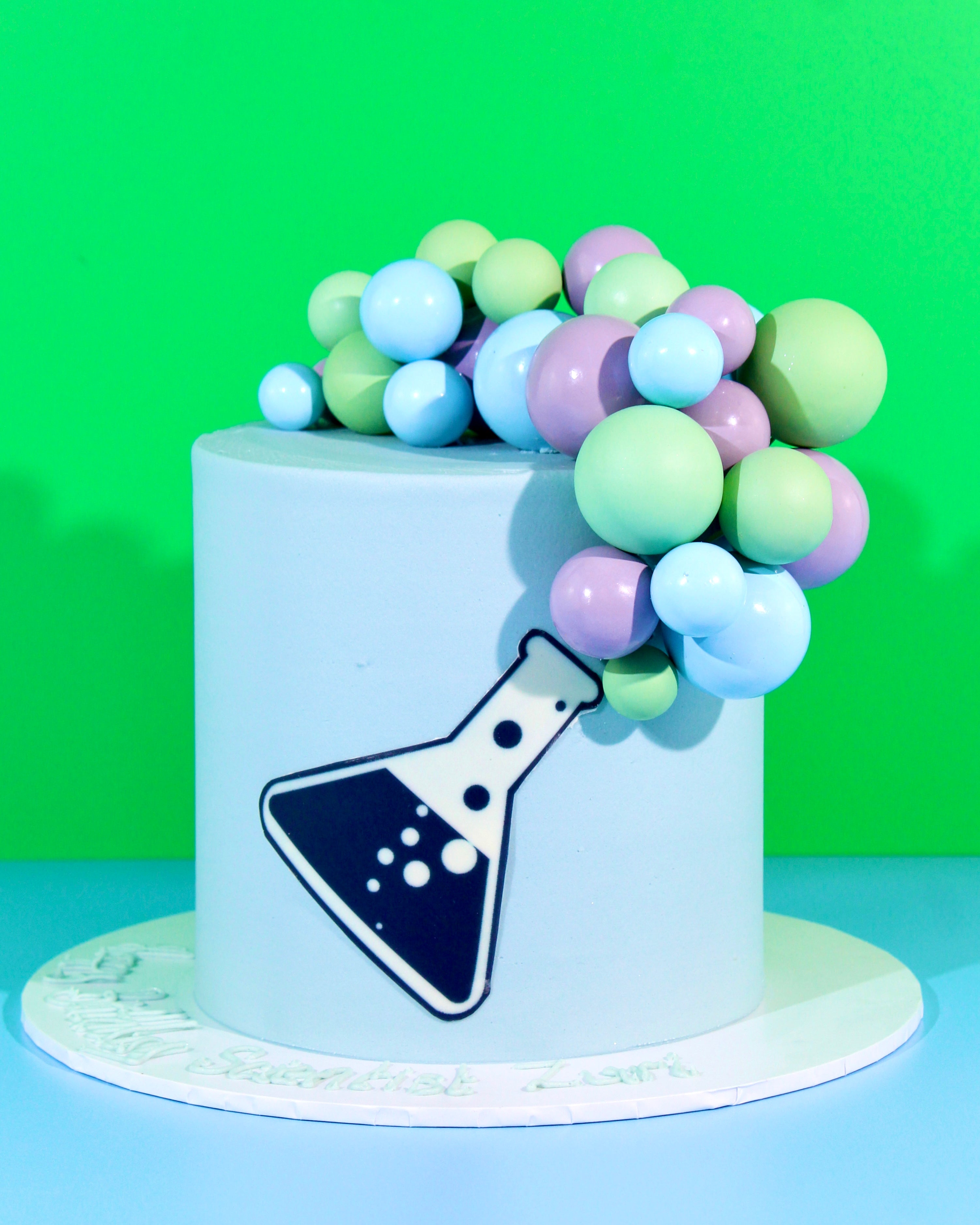 Pastel science-themed cake with chemistry beaker topper and cascading colourful sphere decorations