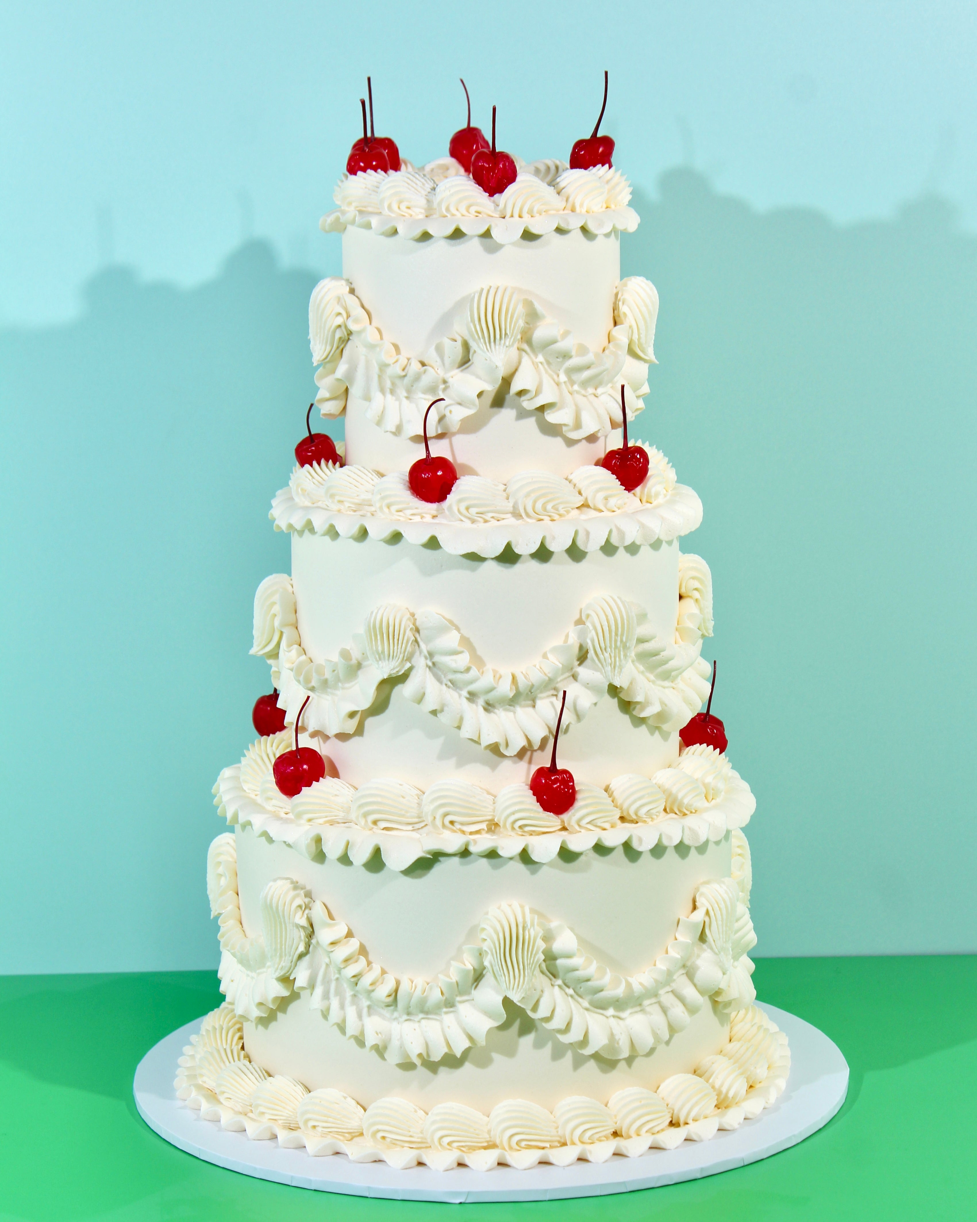 Multi-tier vintage wedding cake decorated with piped buttercream frills and red cherries on a white cake stand.