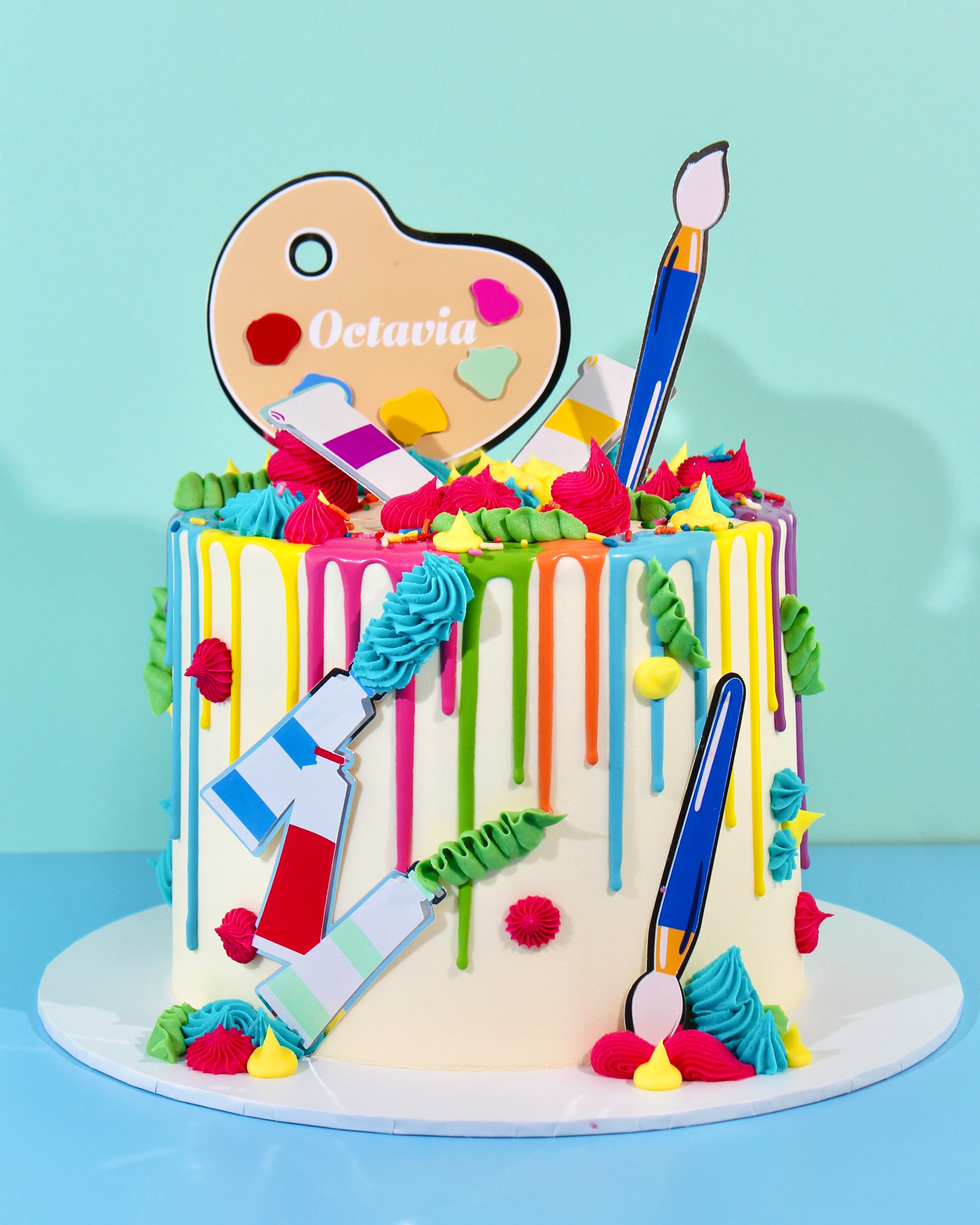 Colourful arts and crafts cake with rainbow drip, piped buttercream swirls, and paintbrush and palette toppers