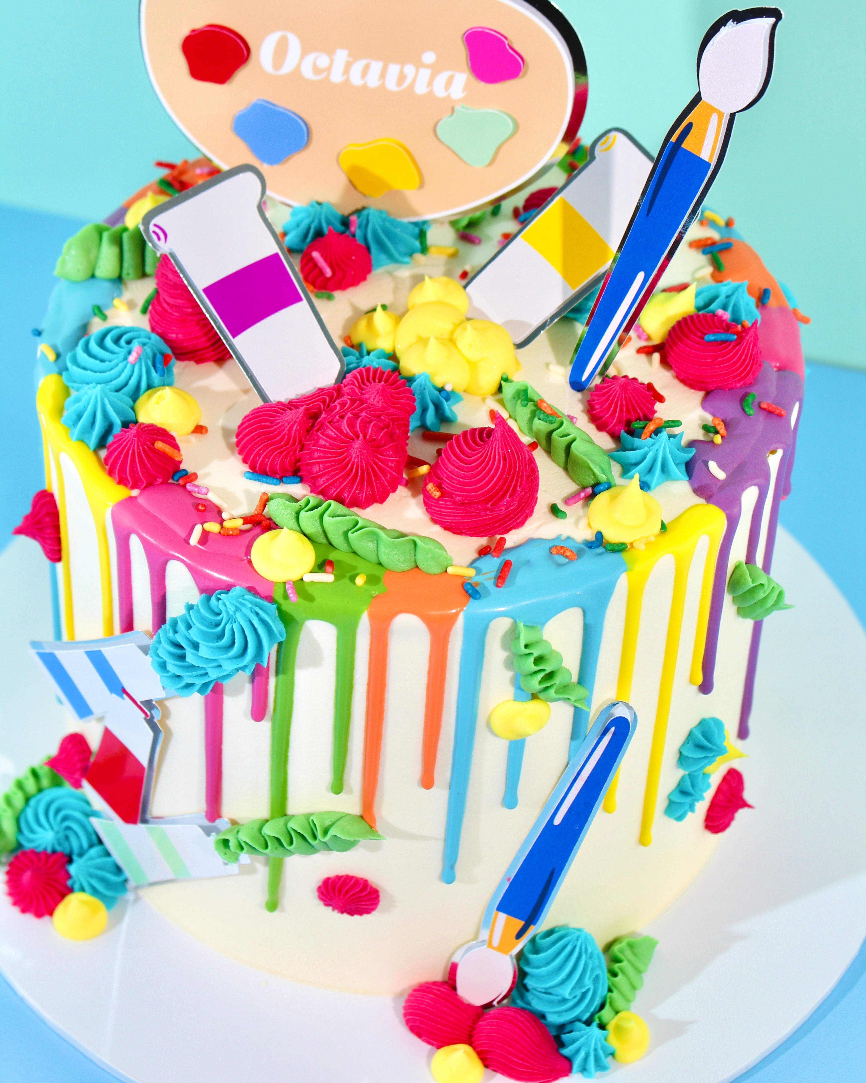 Colourful arts and crafts cake with rainbow drip, piped buttercream swirls, and paintbrush and palette toppers