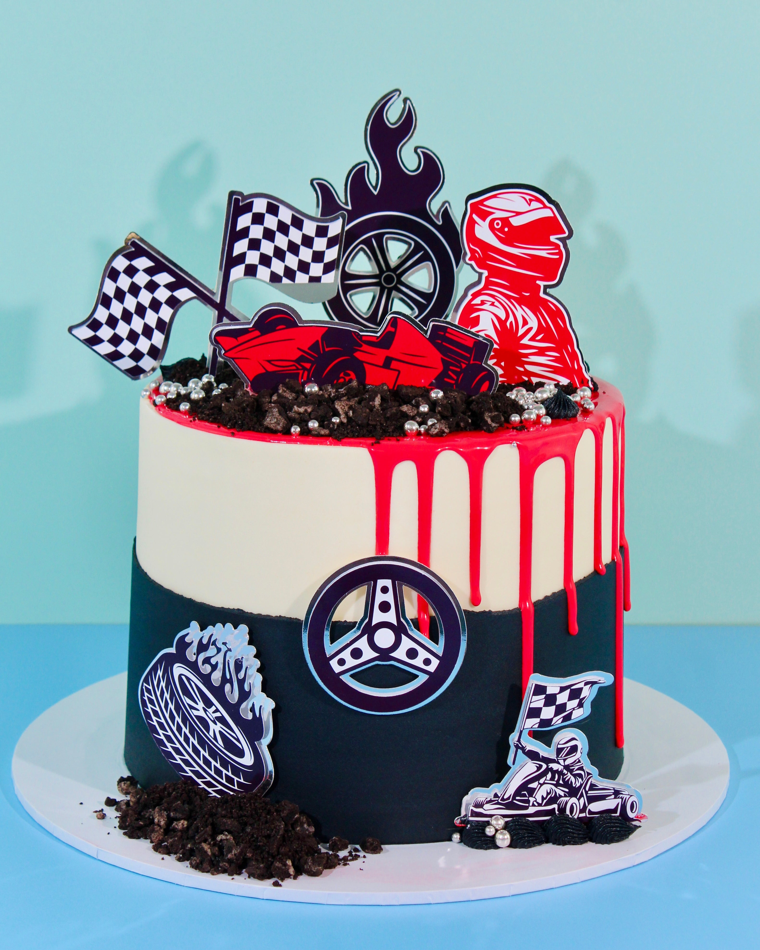 Race car birthday cake with racing driver toppers, red drip, black buttercream, checkered flags and customisable motorsport decorations.