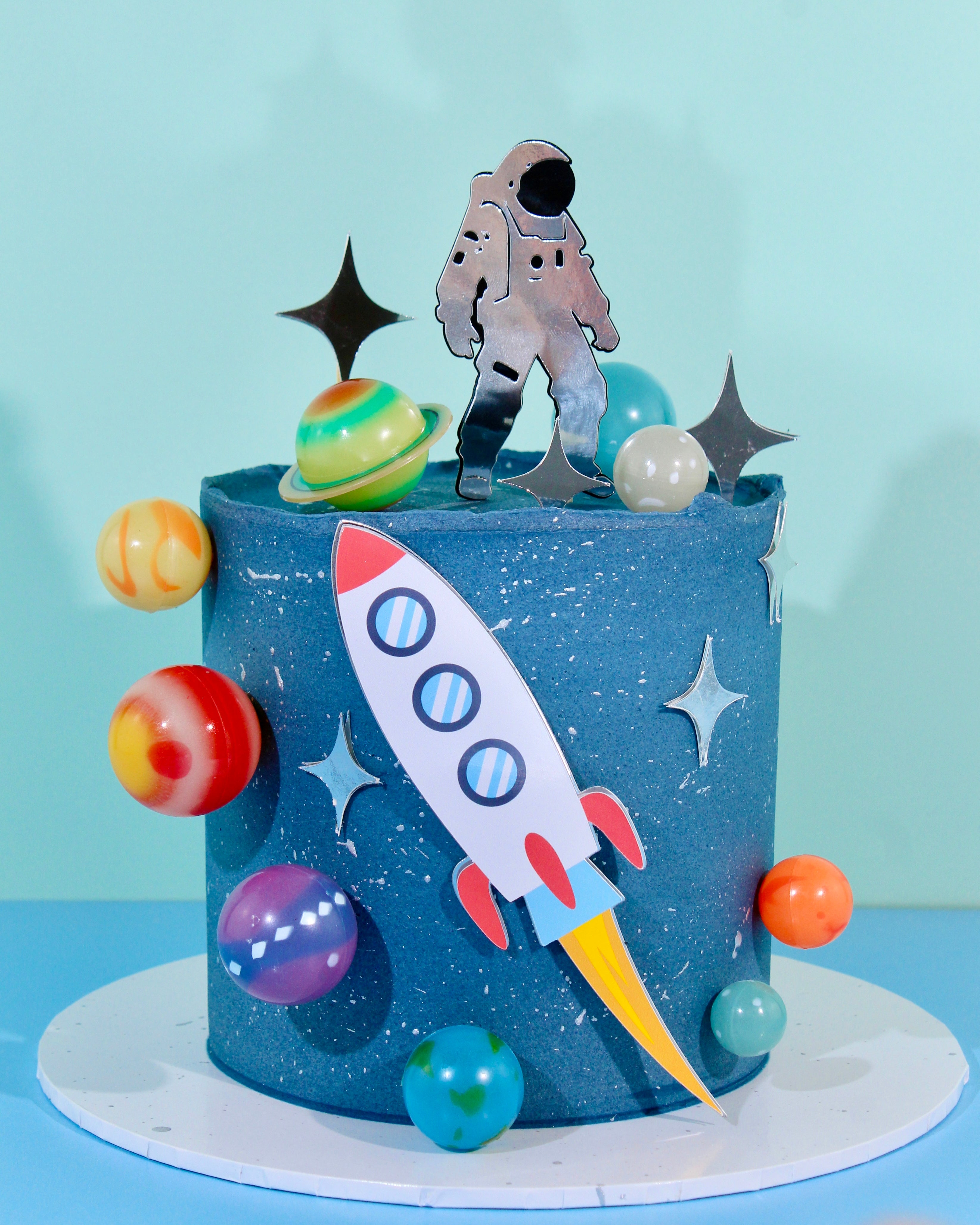 Blue space-themed birthday cake with astronaut topper, rocket and planets by Amy’s Bakehouse.