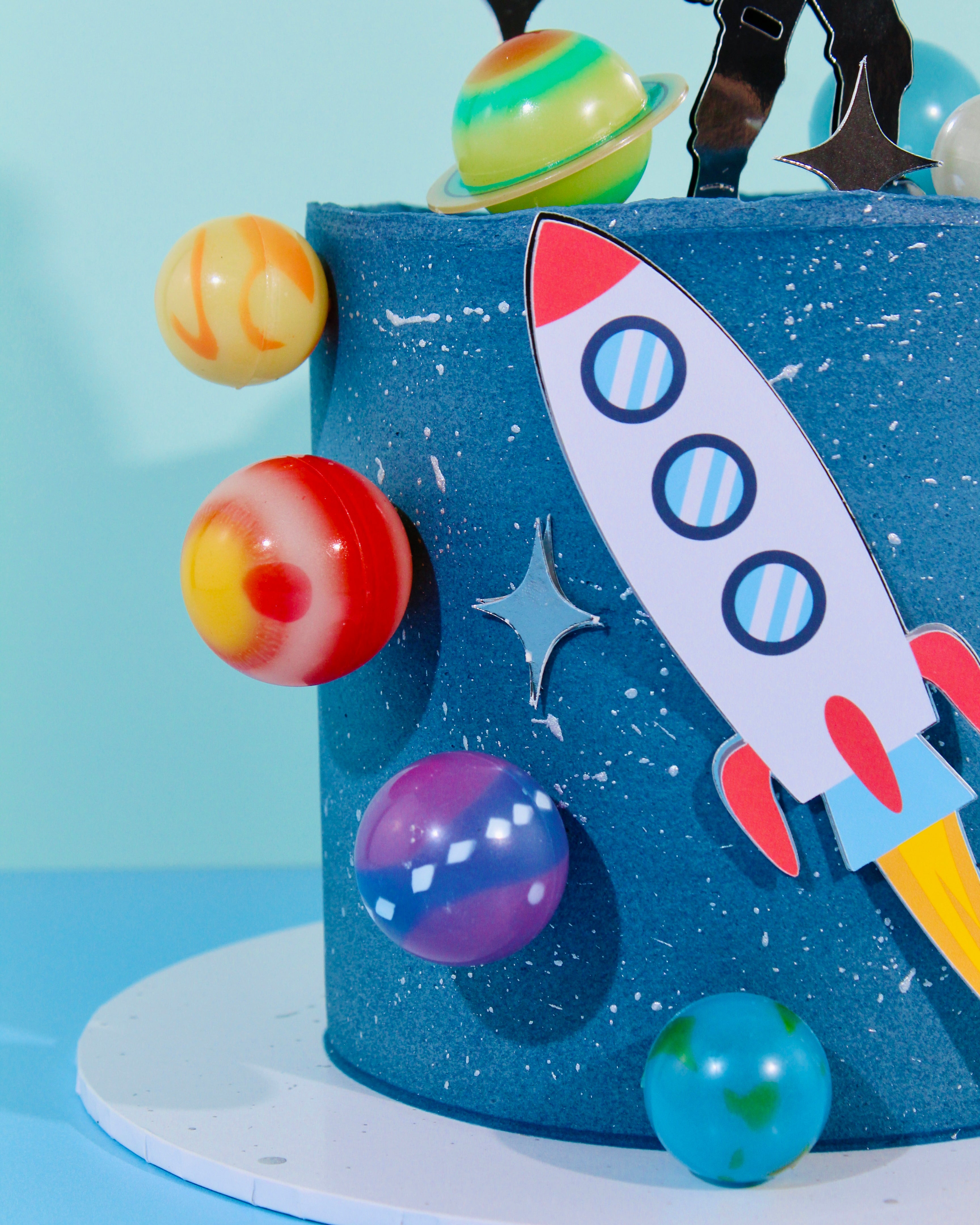 Blue space-themed birthday cake with astronaut topper, rocket and planets by Amy’s Bakehouse.