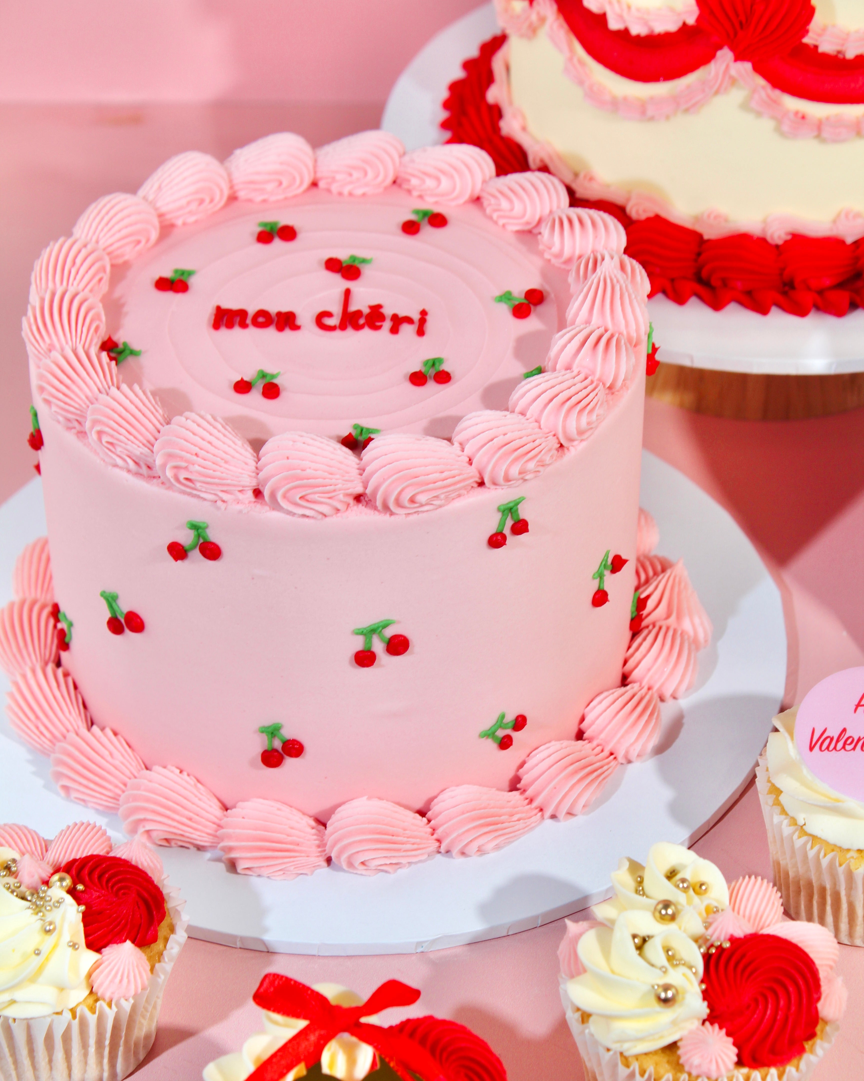 Pink Mon Chèri cake with cherry detailing and piped buttercream border