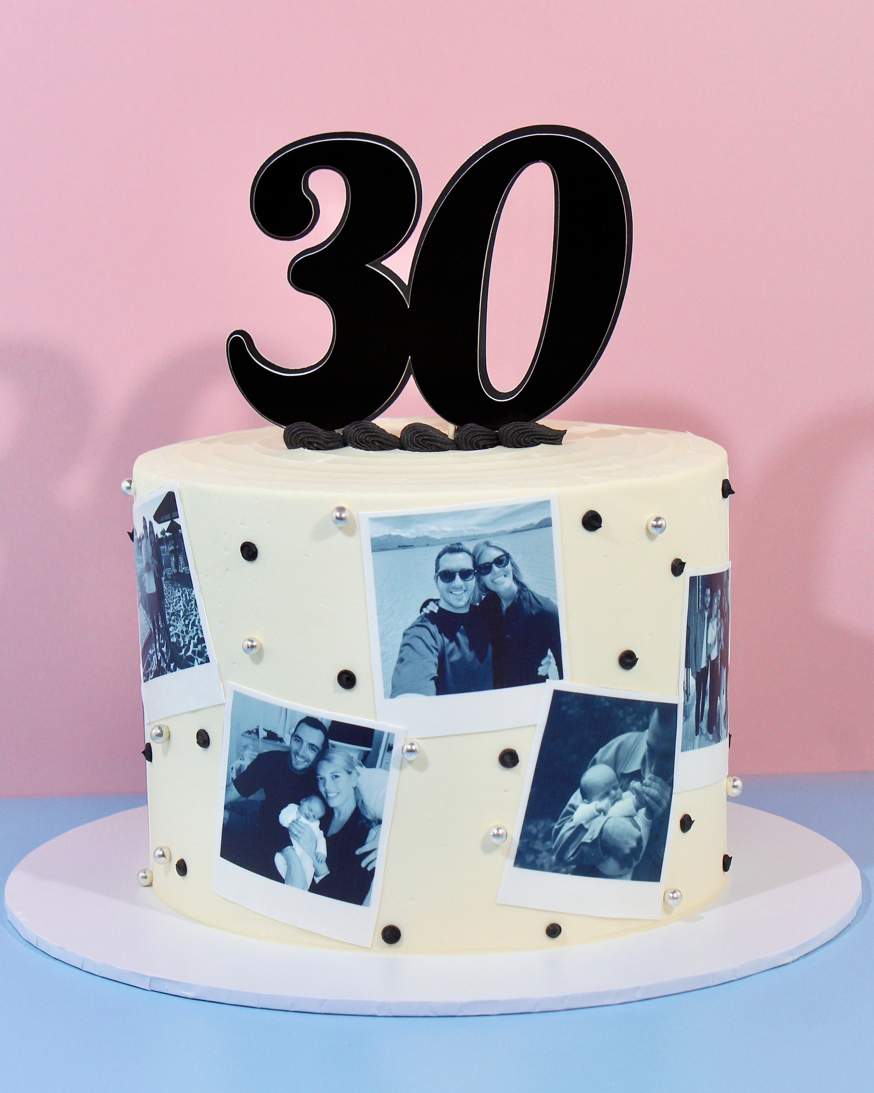 Ivory birthday cake decorated with black and white polaroid photo prints and a bold 30 number topper