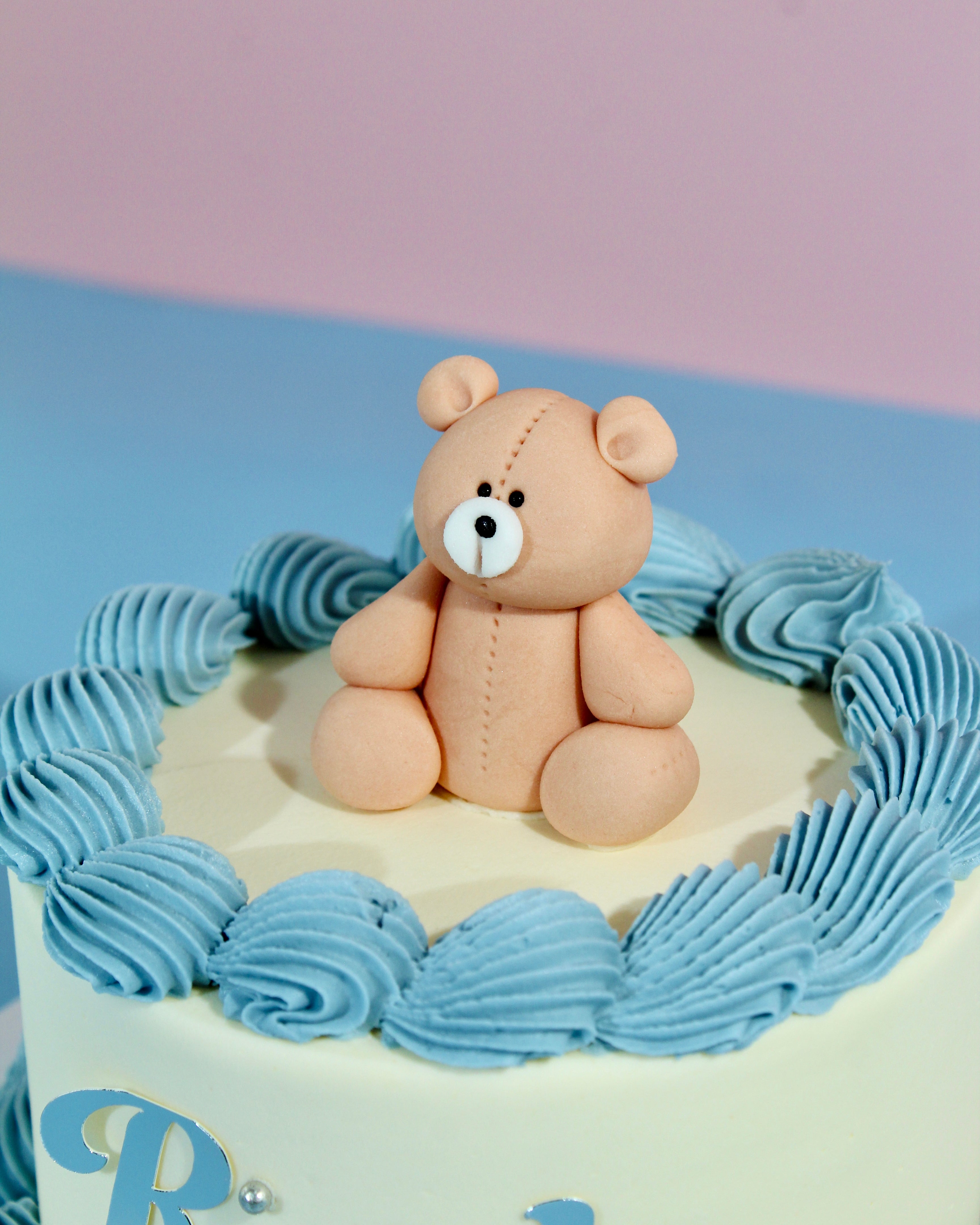 Teddy bear cake topper on a cake with blue frosting