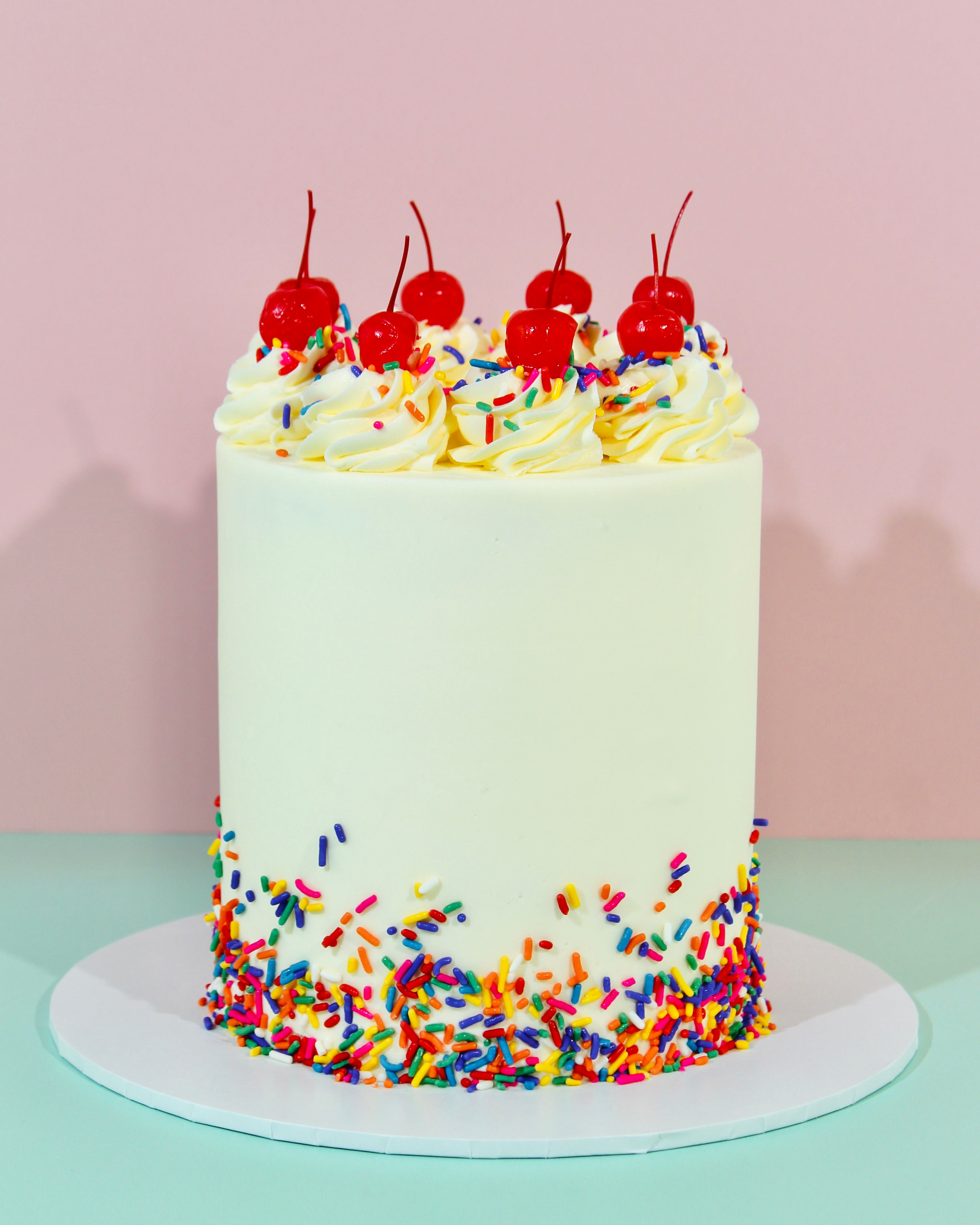 Vanilla sprinkle cake with buttercream swirls, rainbow sprinkles and cherries on top