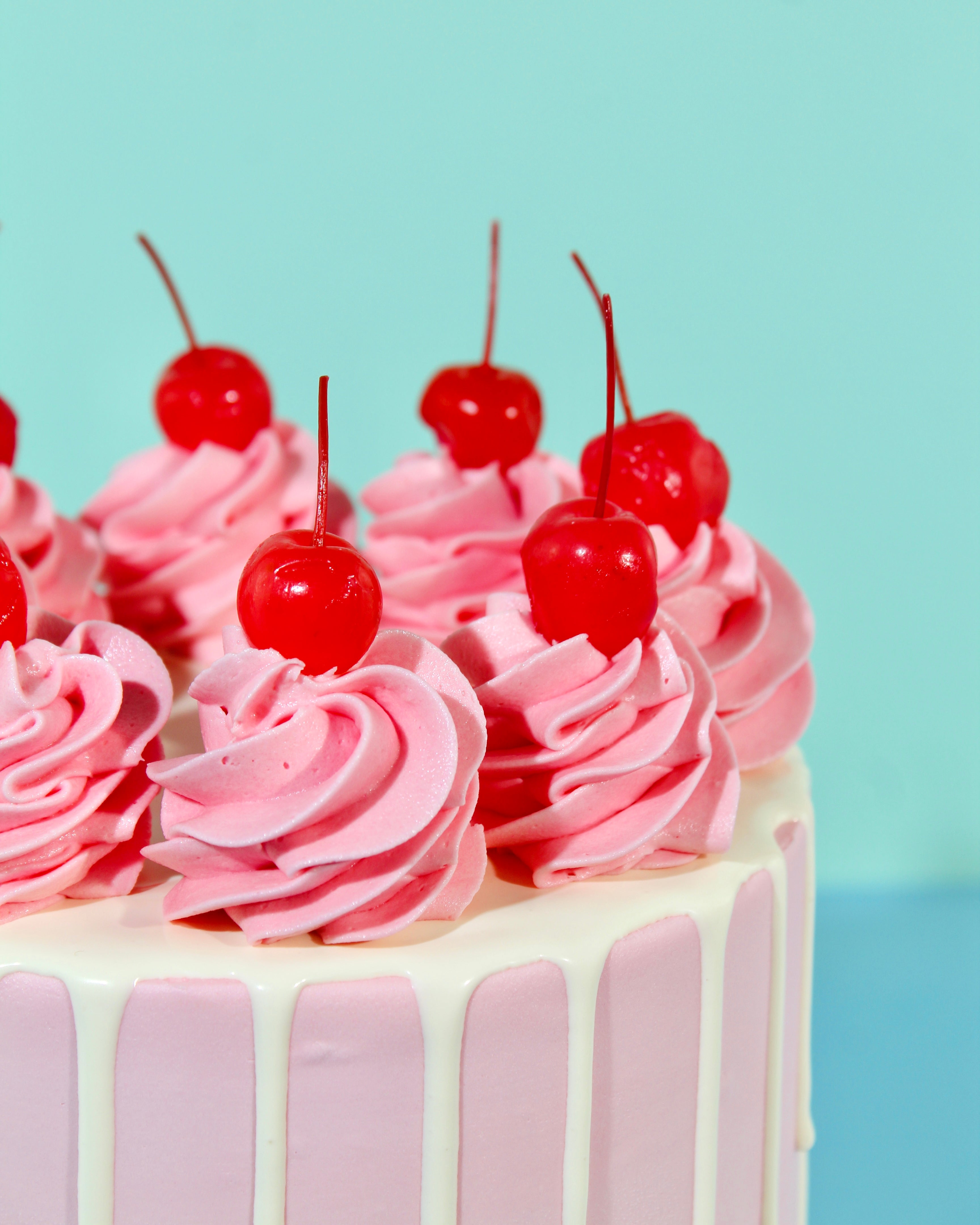Close up of pink buttercream swirl cake with white drip icing and bright red cherries