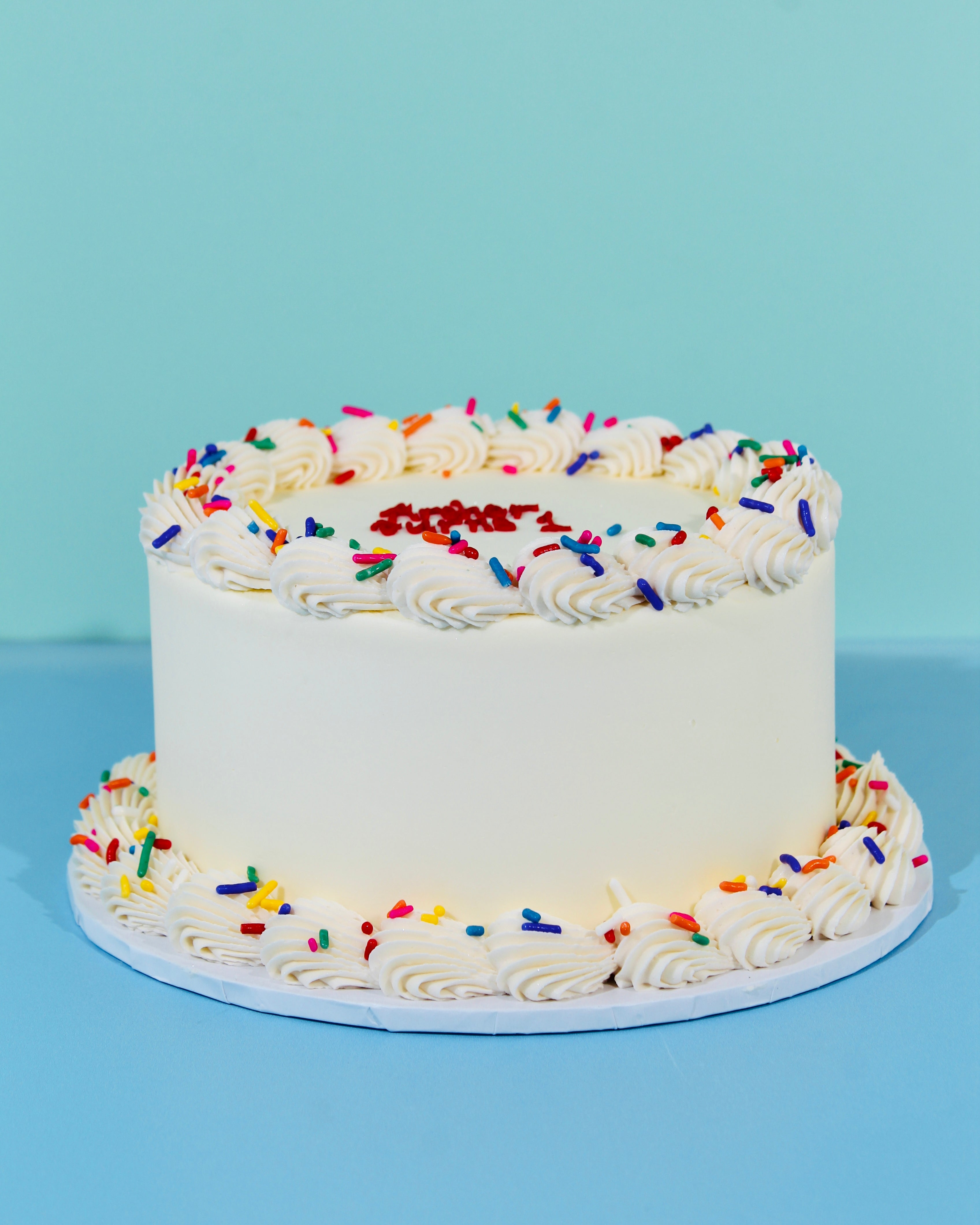 Mini white buttercream cake with piped borders and colourful rainbow sprinkles