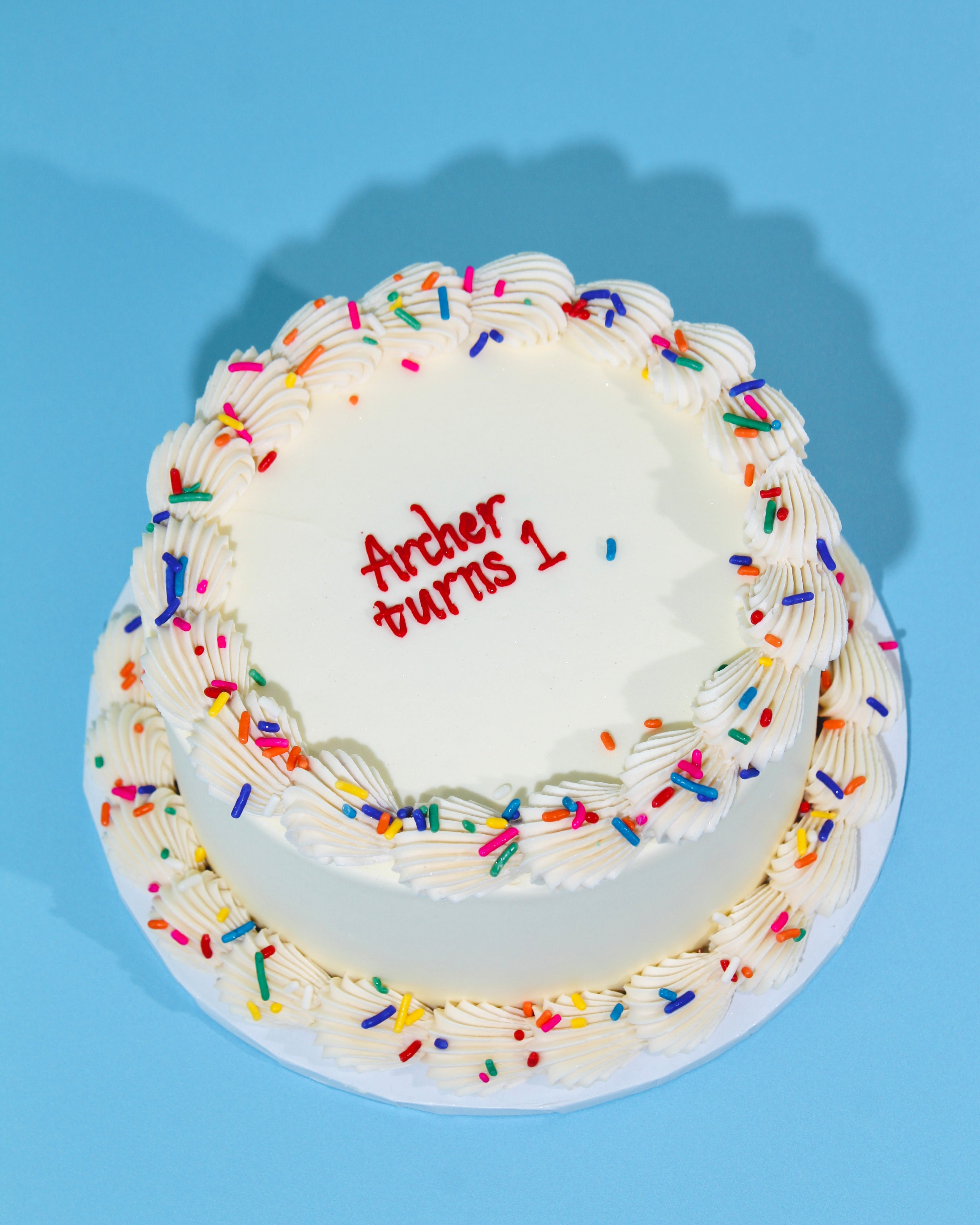Small round cake with white frosting, colorful sprinkles, and 'Arthur turns 1' text on a blue background.