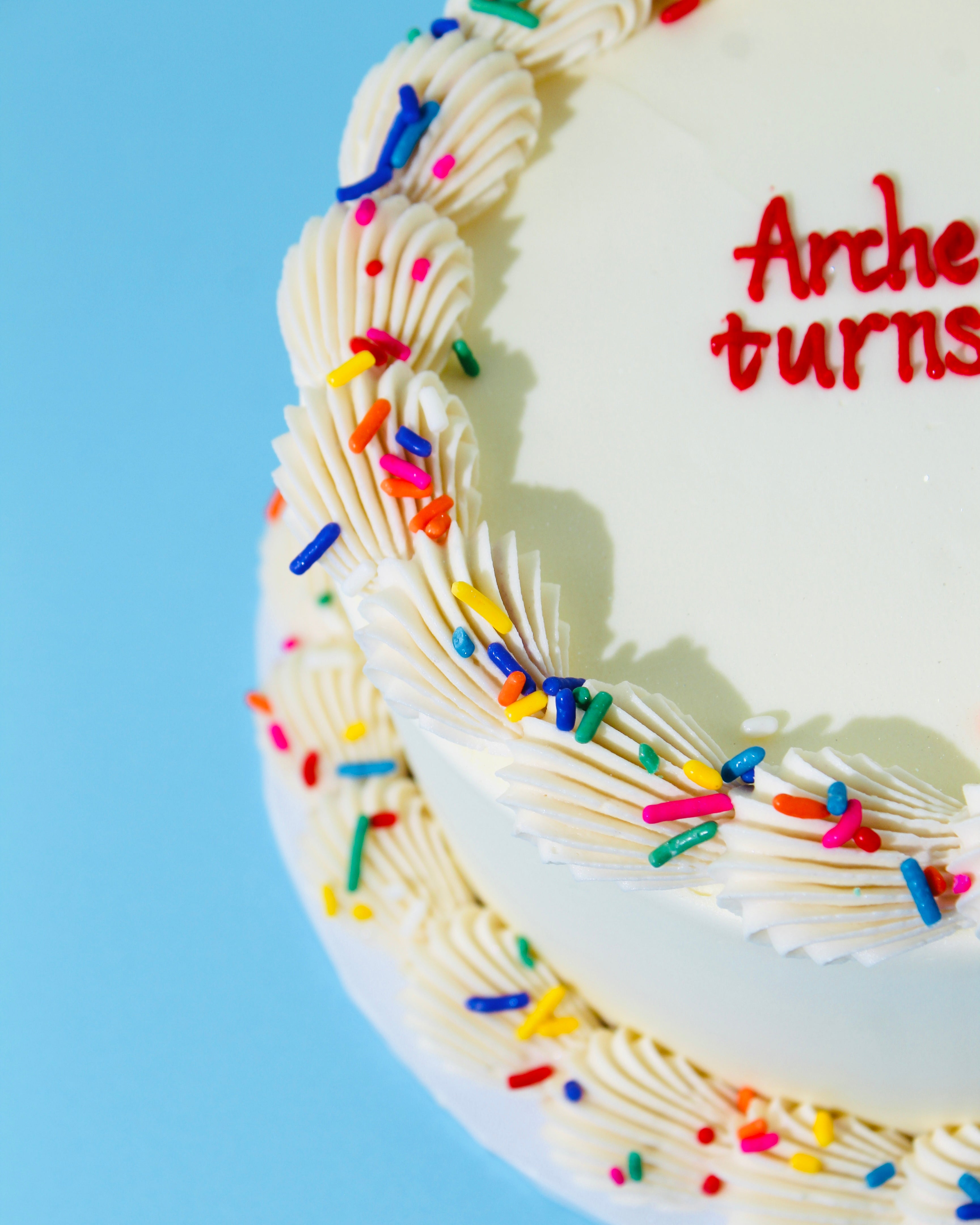 Birthday cake with colorful sprinkles and 'Archie turns' text on a blue background