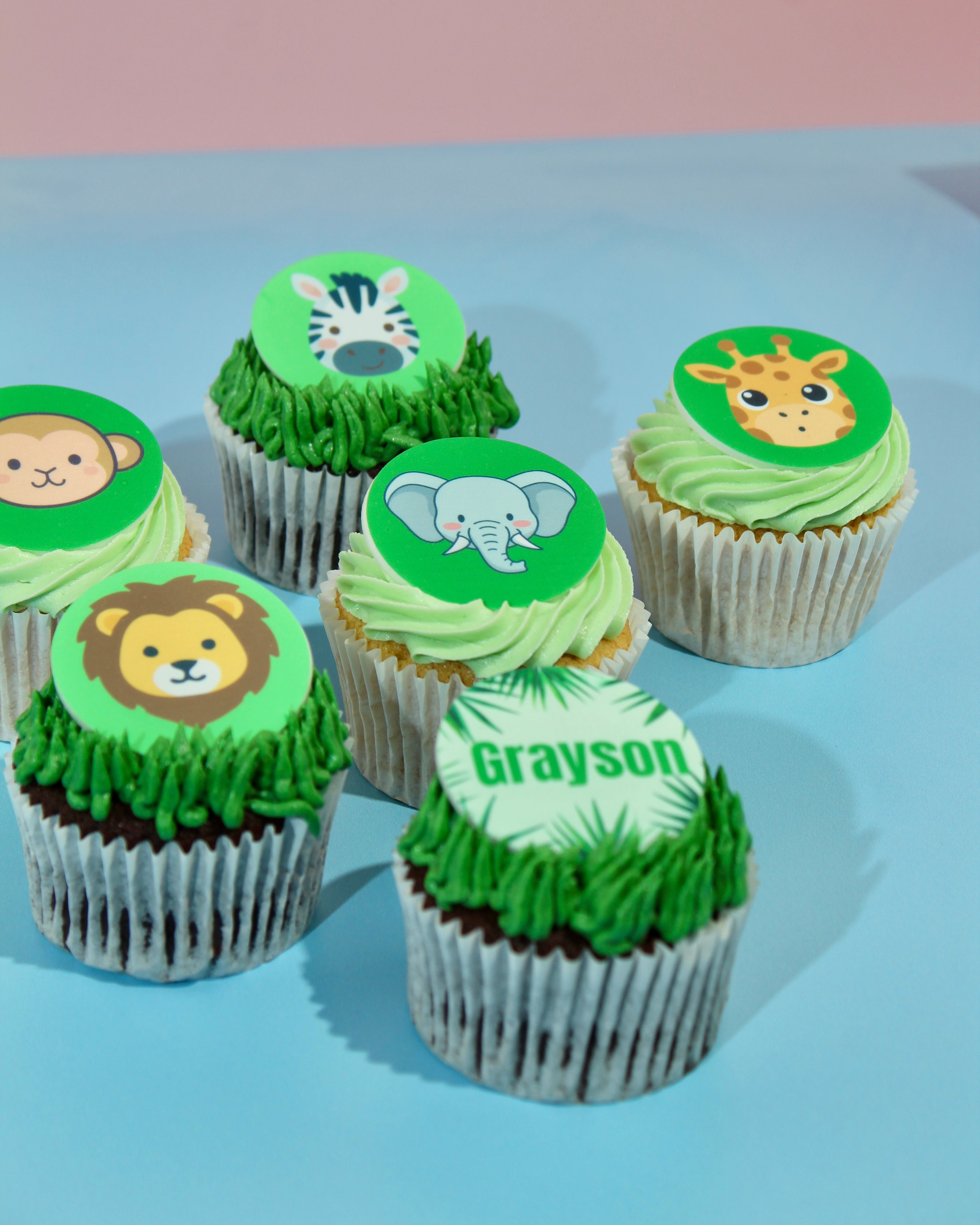 Cupcakes with green frosting and animal-themed toppers on a light blue background