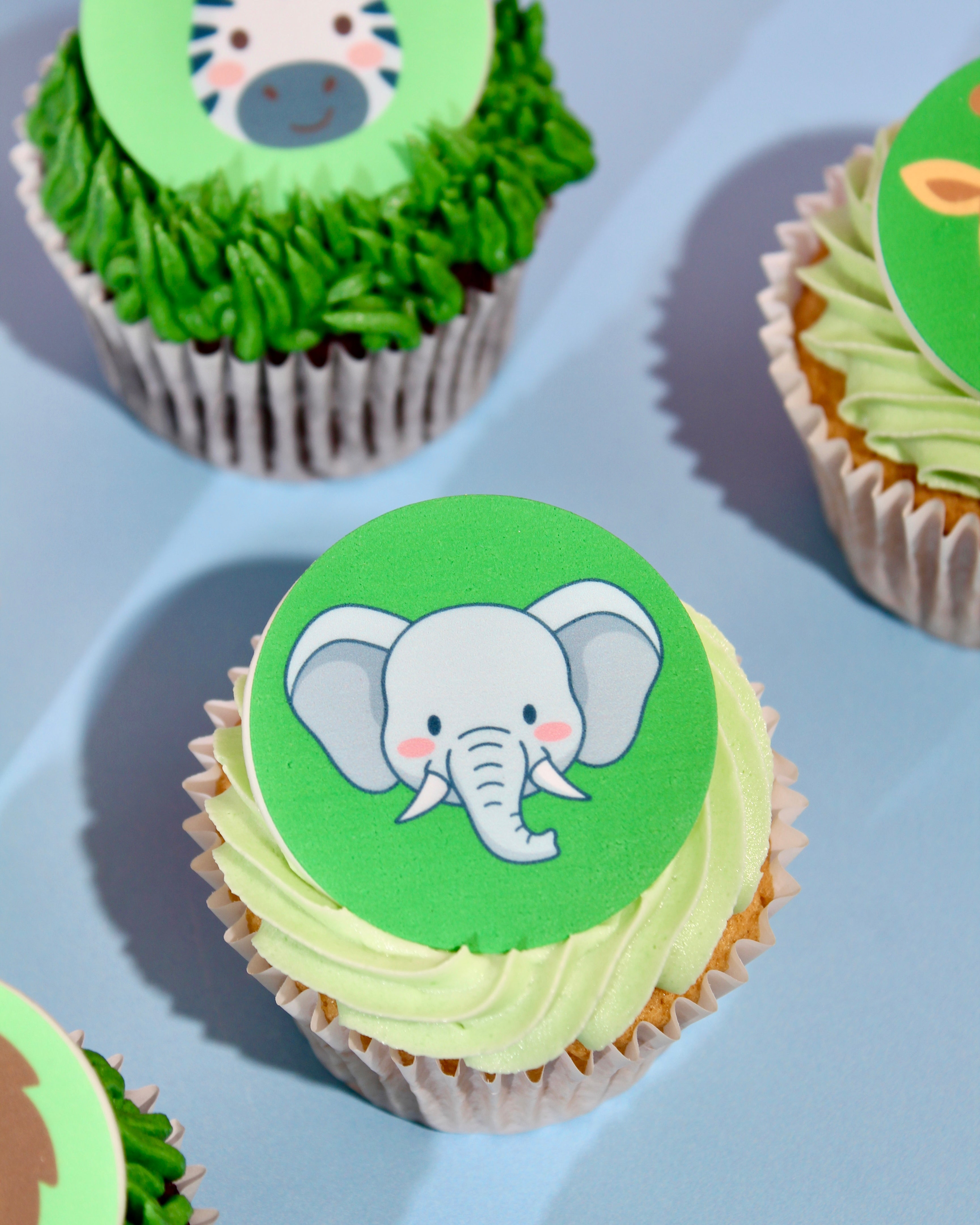 Cupcakes with green frosting and animal-themed toppers on a light blue background