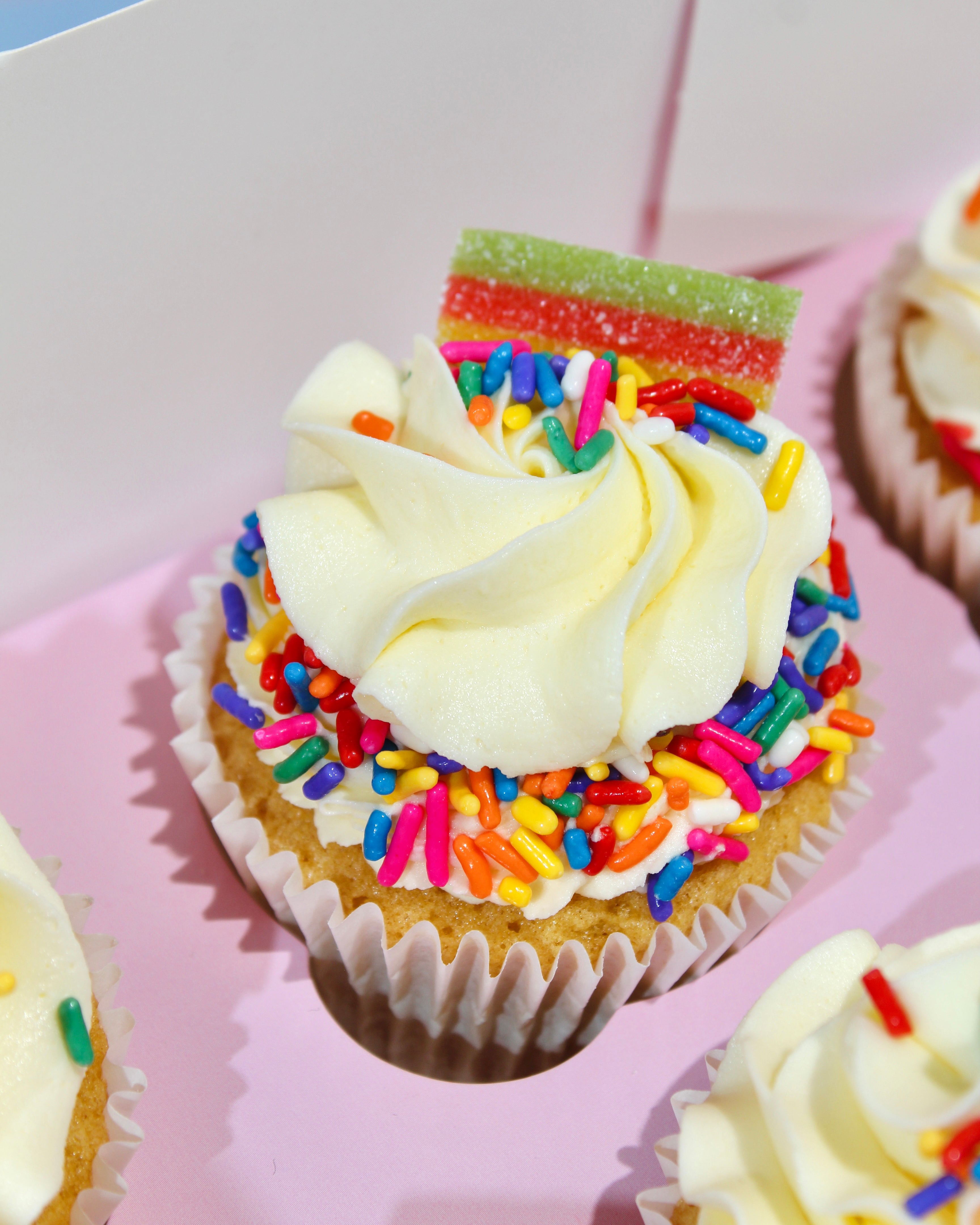 Cupcake with white frosting and colorful sprinkles on a pink tray