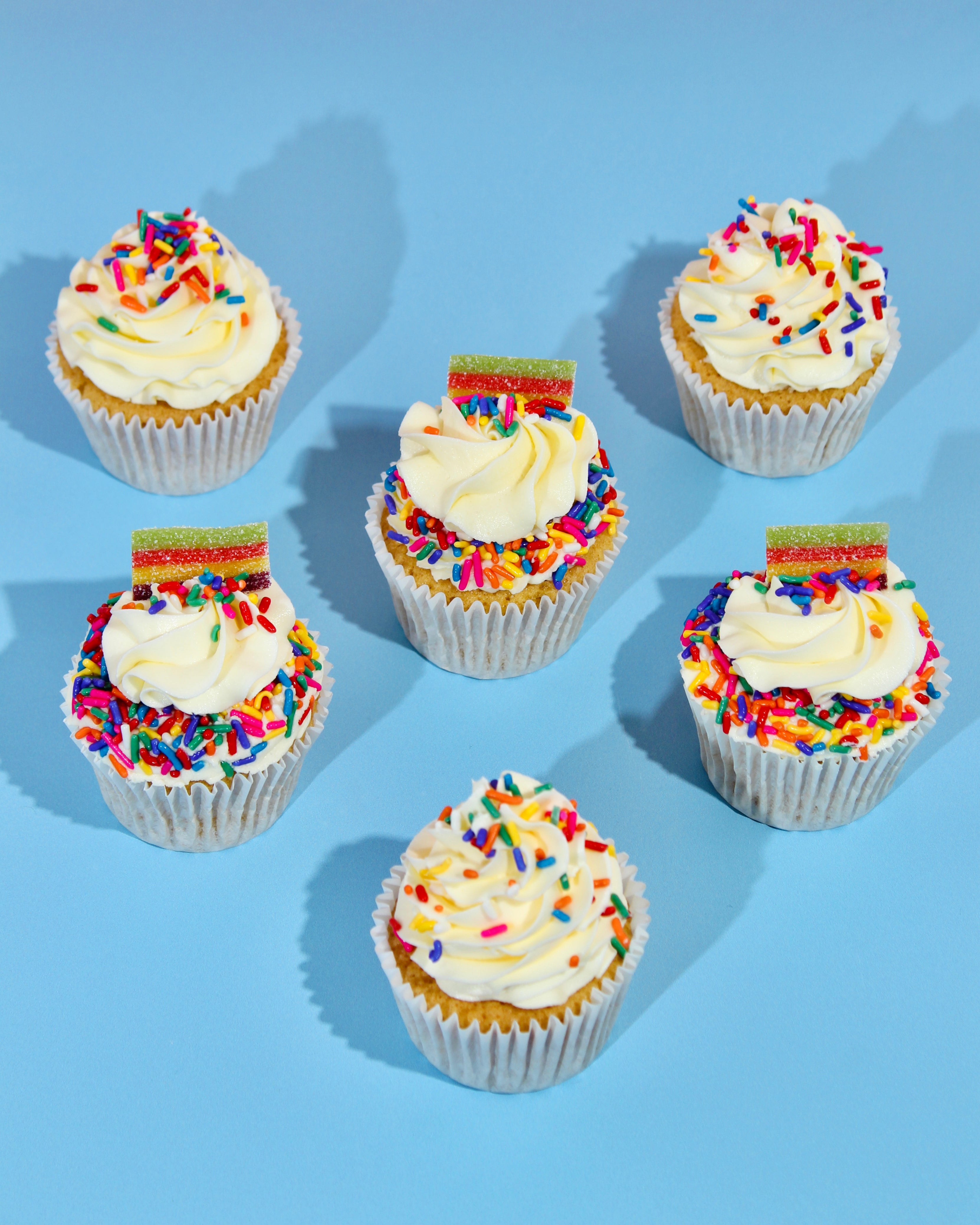 Six cupcakes with white frosting and colorful sprinkles on a blue background