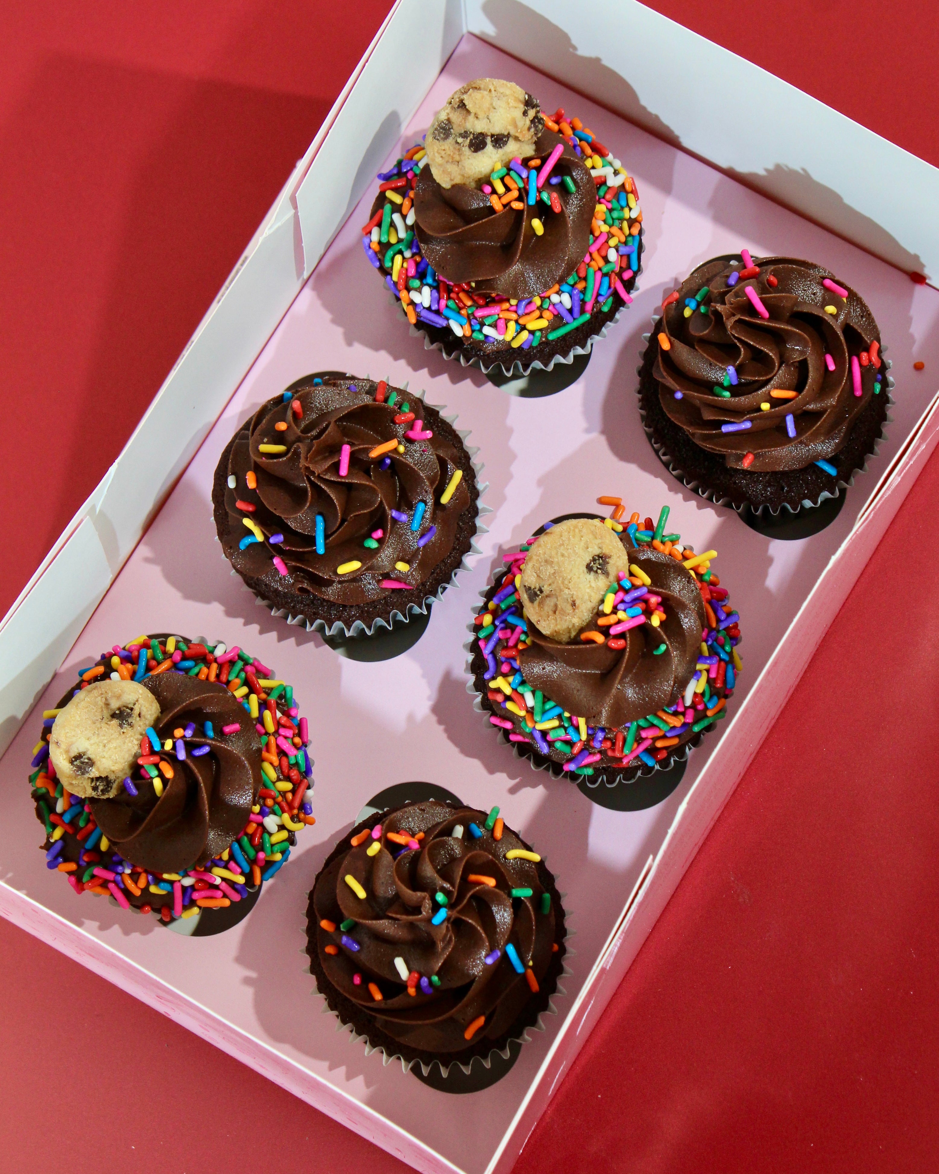 Chocolate cupcakes with chocolate buttercream, rainbow sprinkles and mini cookie topper in a box