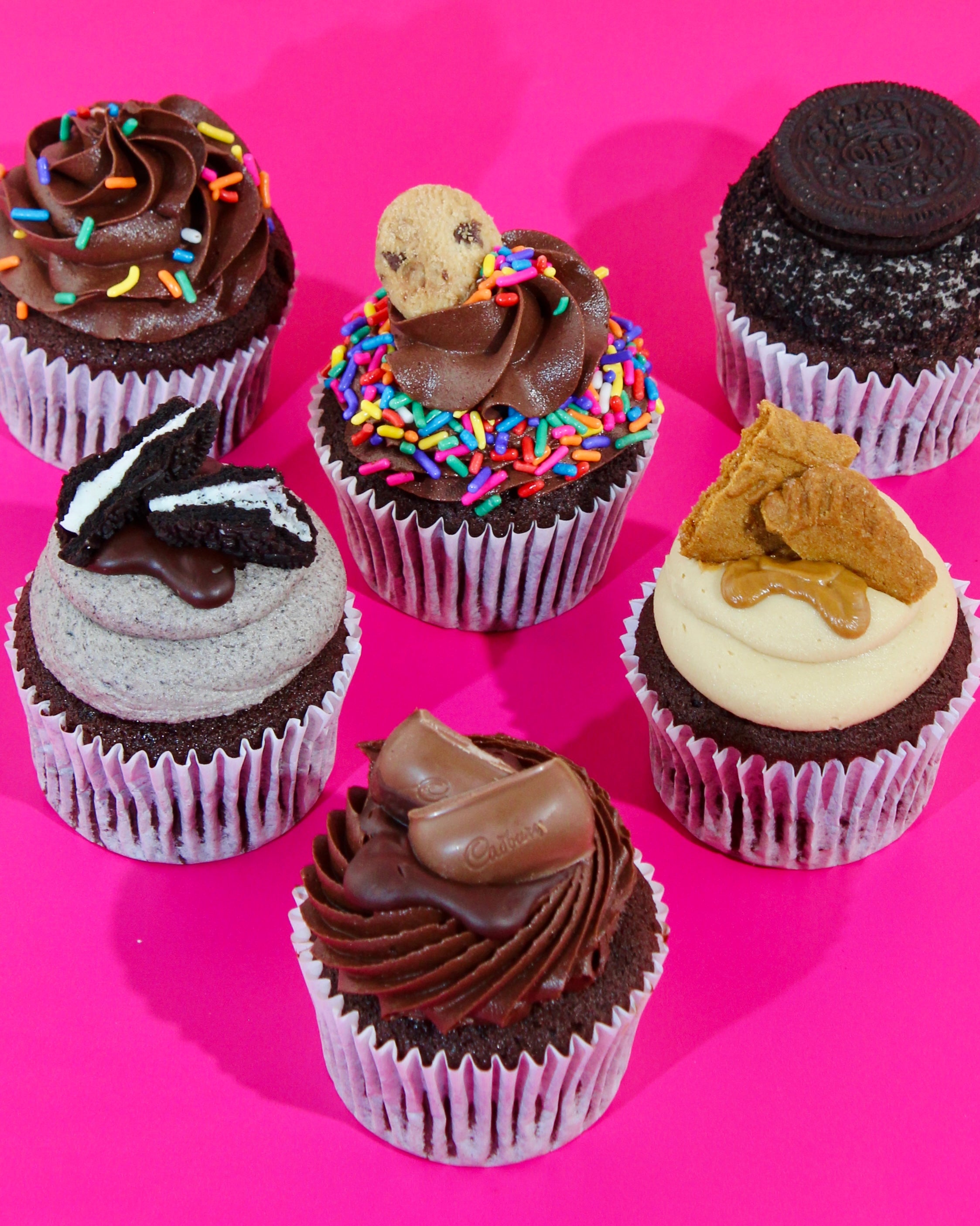 Mixed cupcake box with Oreo, Biscoff, Kinder and chocolate cupcakes on pink background