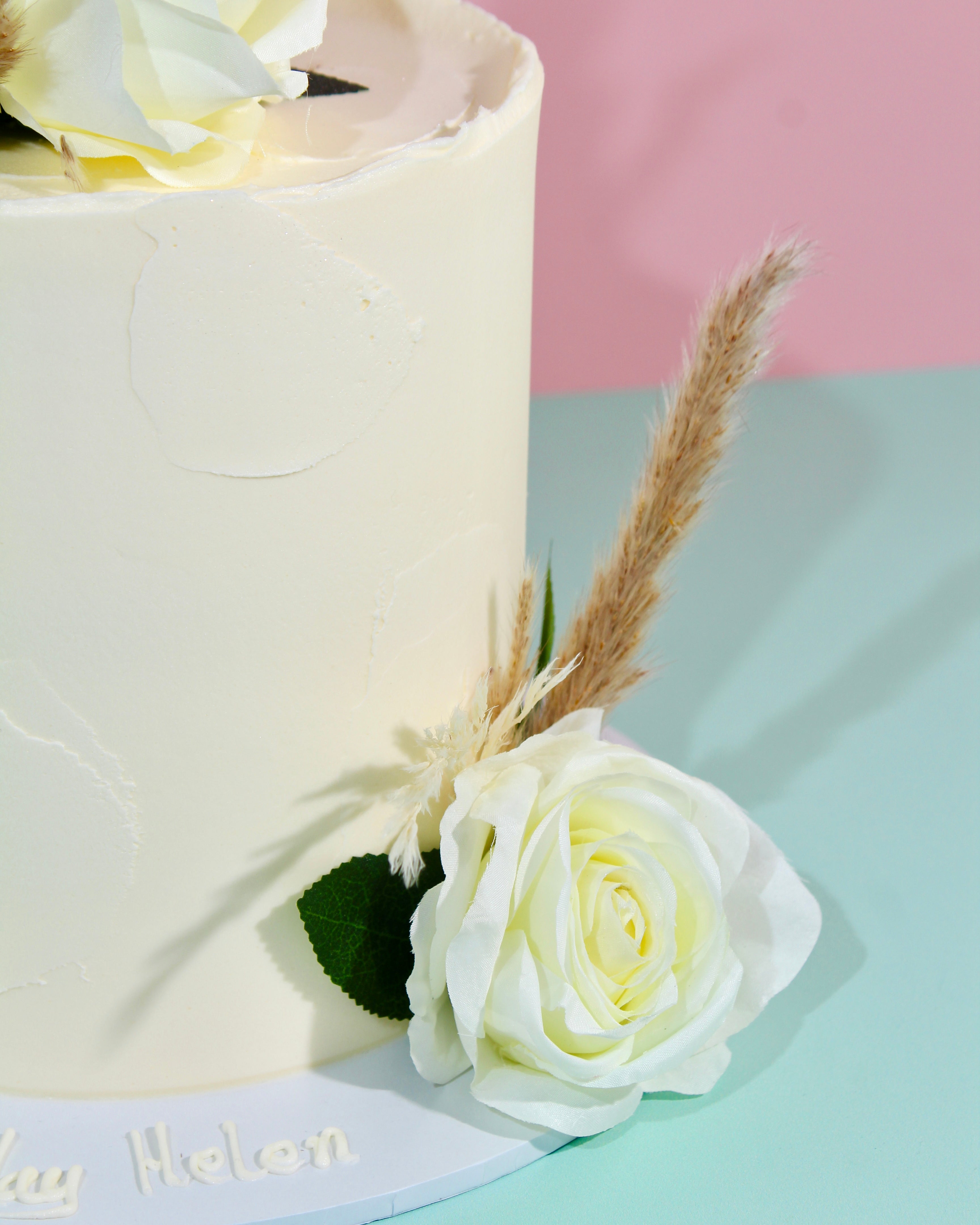 Textured ivory buttercream cake topped with white roses and dried pampas grass, boho wedding cake style
