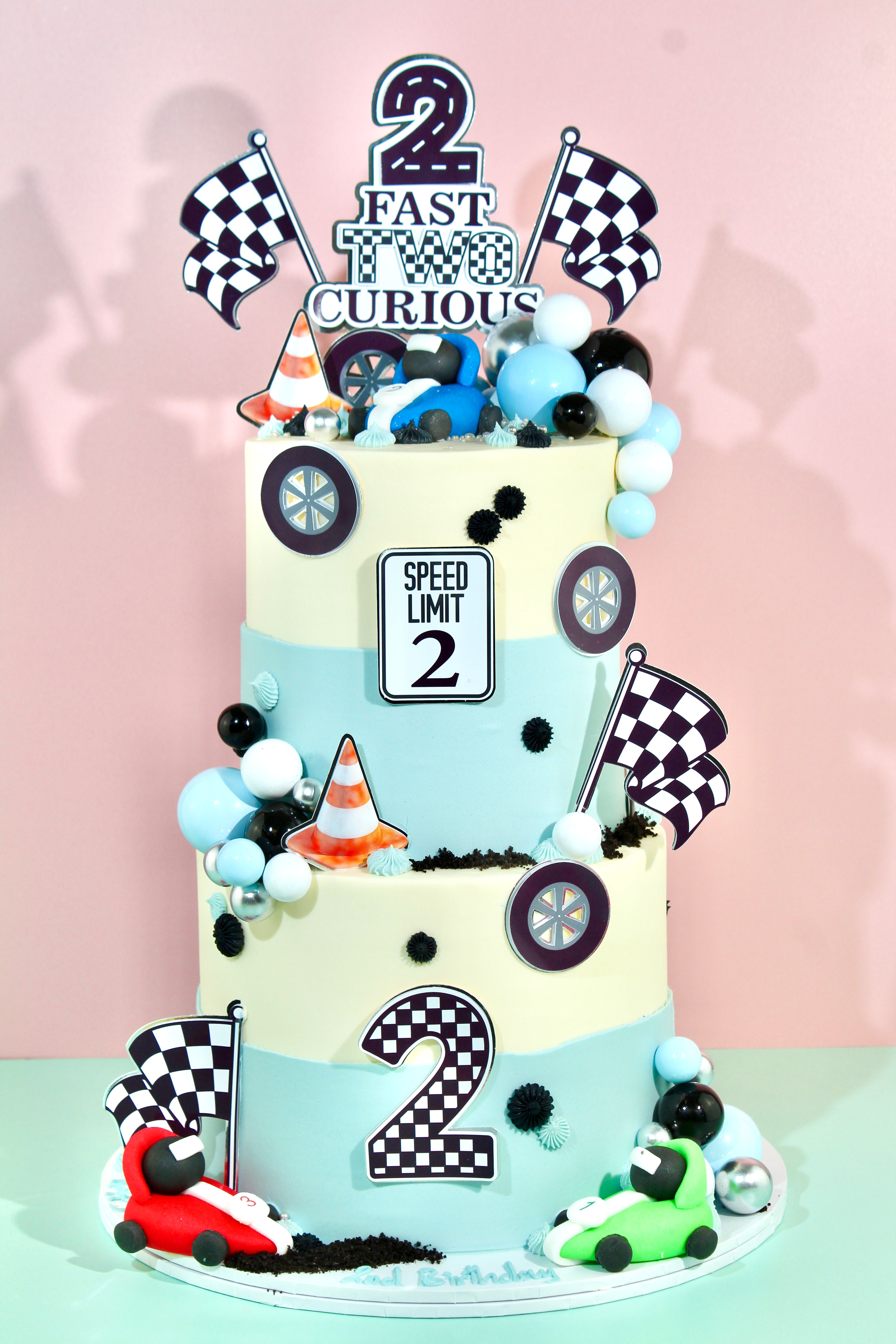 Two-tier racing birthday cake with chequered flags, speed limit sign and race car decorations

