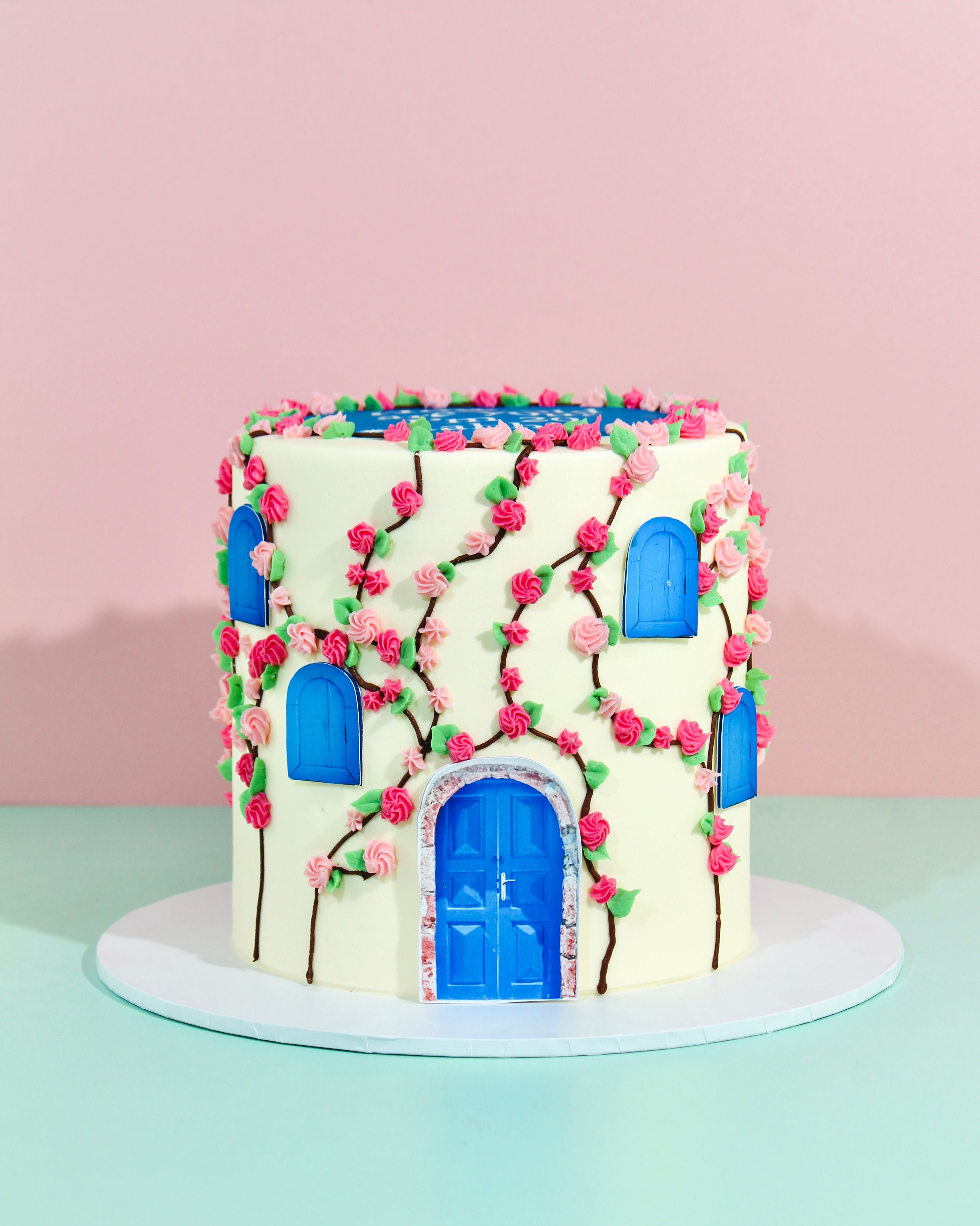 Ivory birthday cake with climbing pink roses, blue arched windows and bold 20th birthday message on top