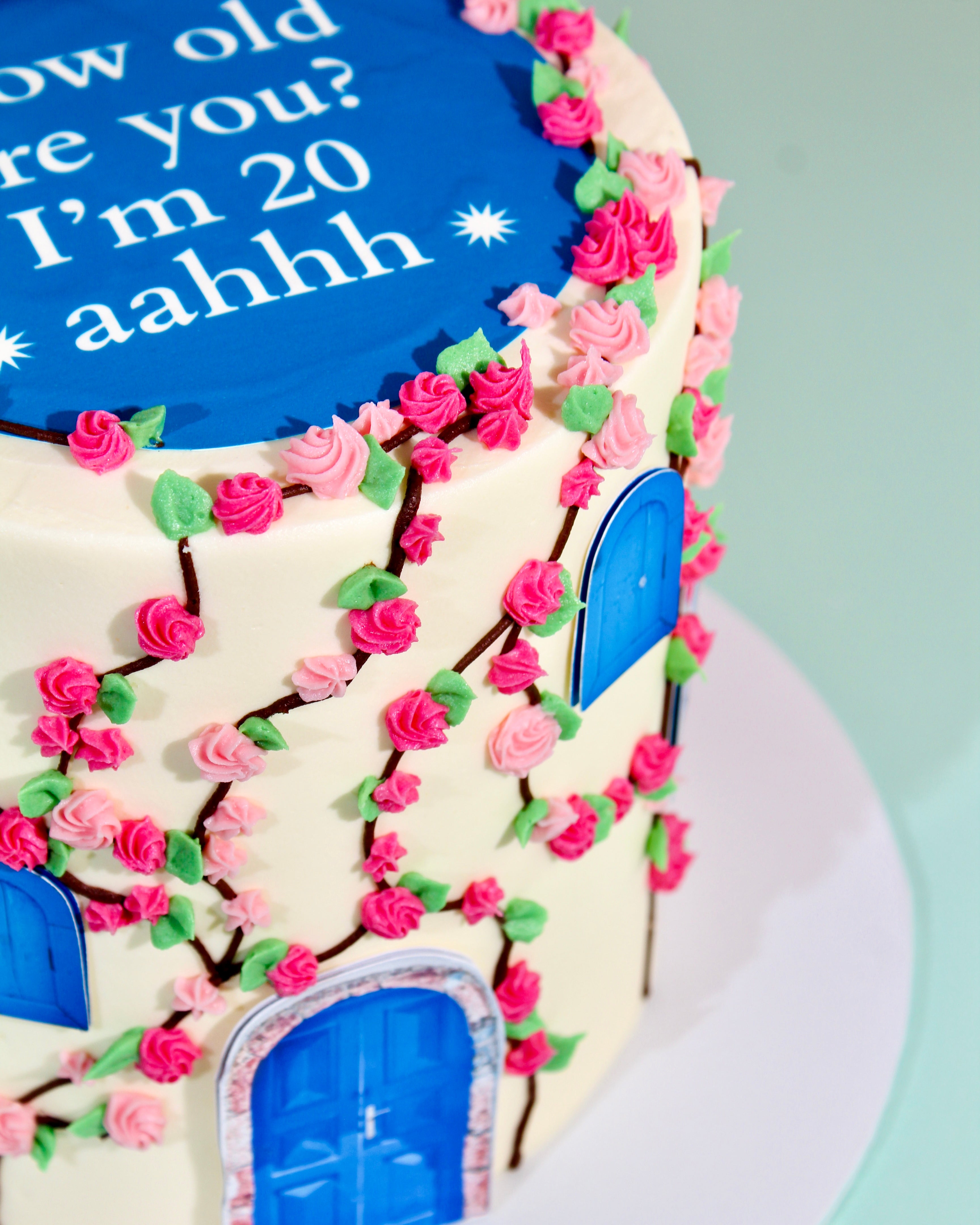 Birthday cake with floral decorations and text 'How old are you? I'm 20 aahhh' on a blue background