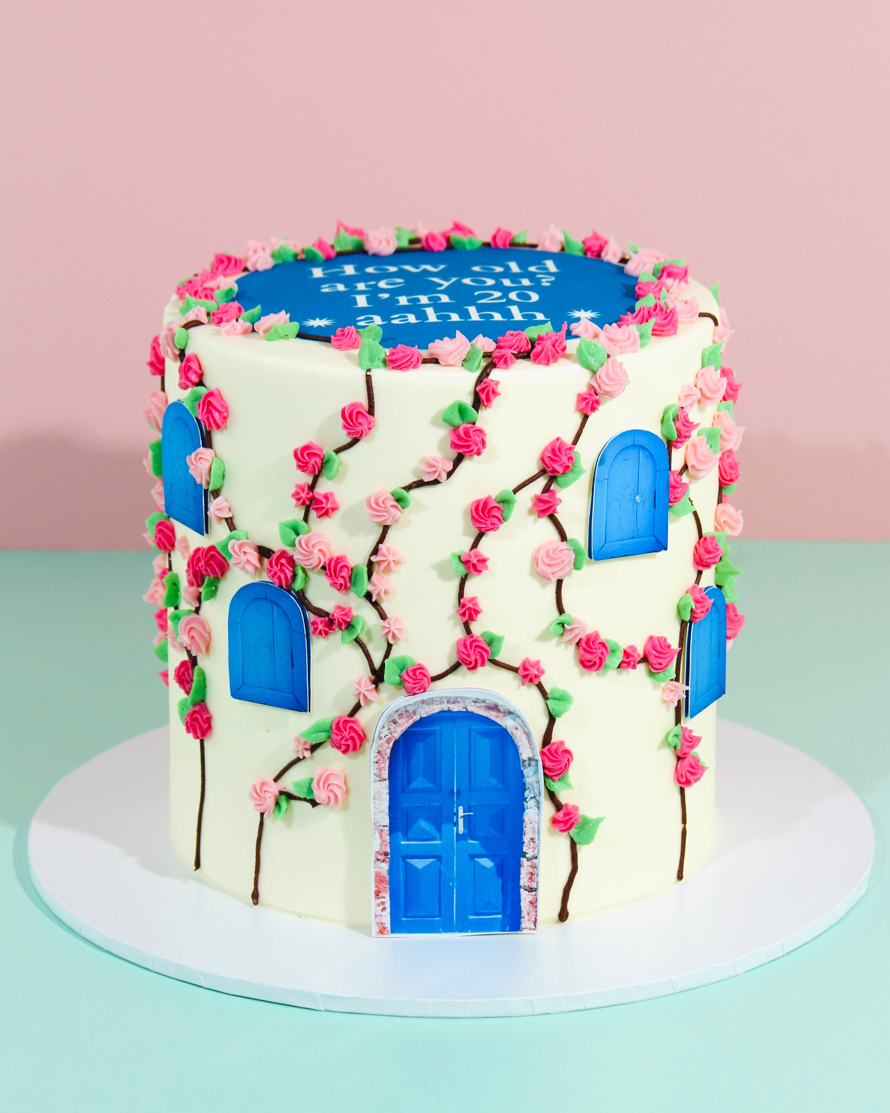 Decorative cake shaped like a house with blue doors and pink flowers on a light green background