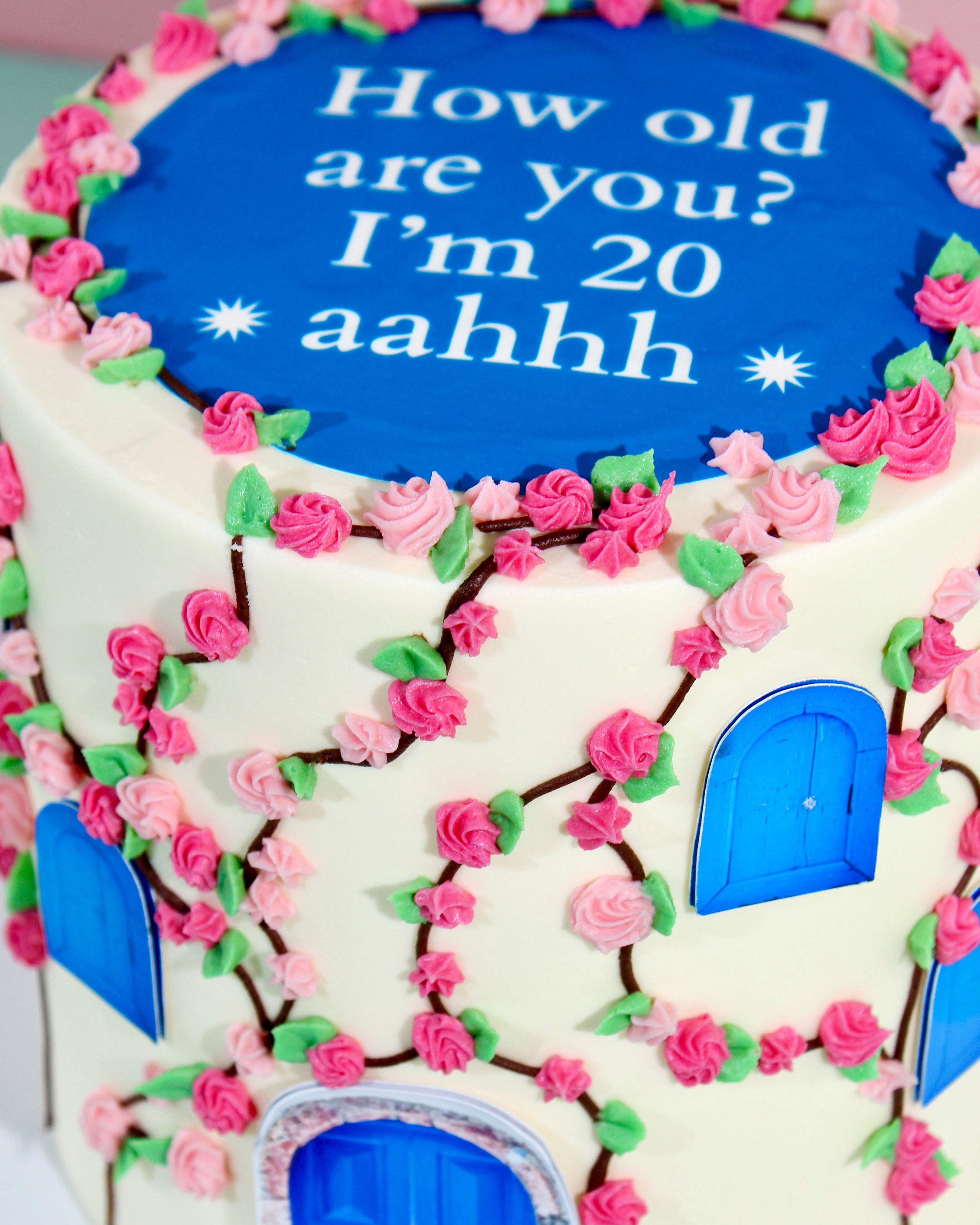 Decorative cake with blue door and pink flowers, featuring text 'How old are you? I'm 20 aahhh'.