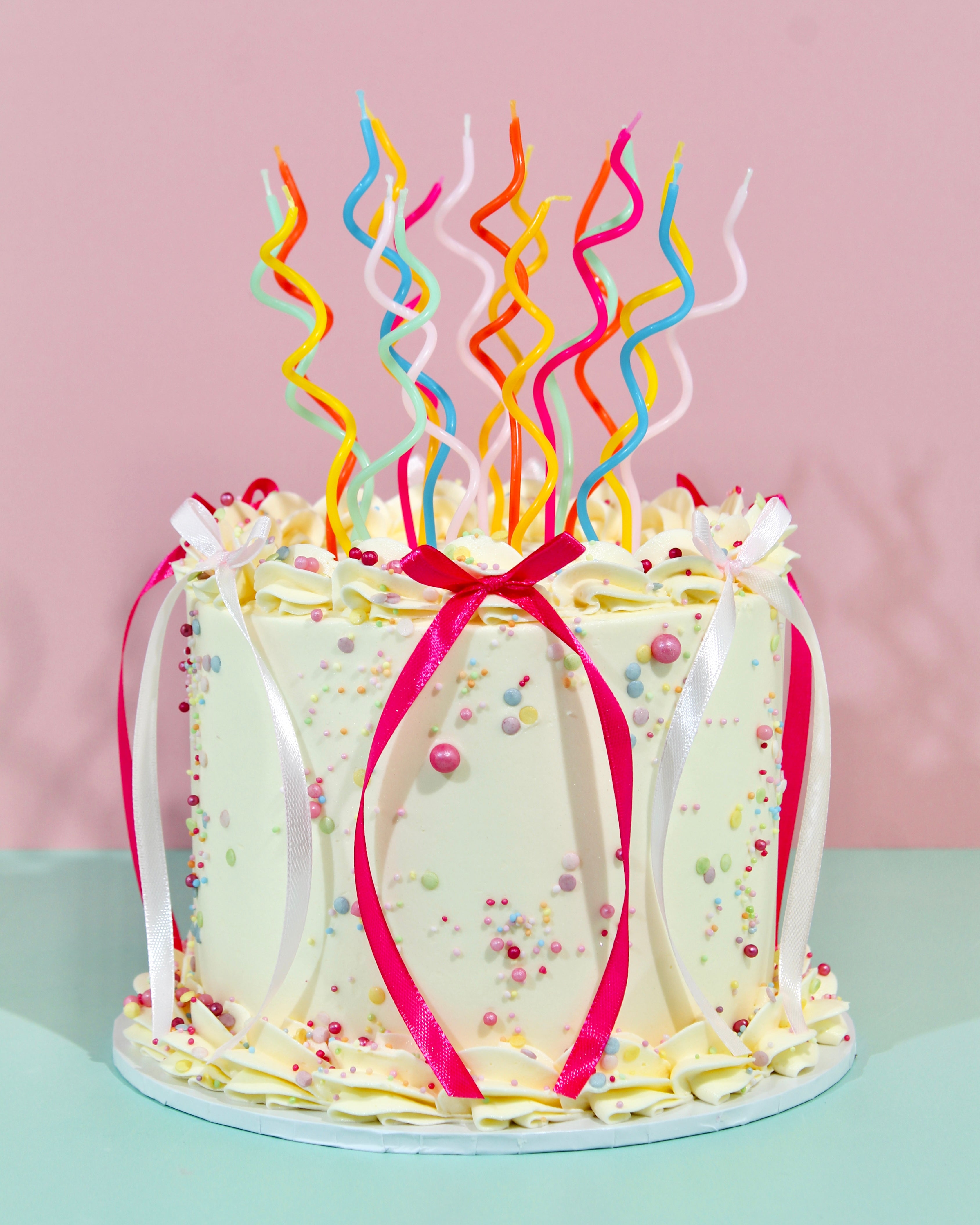 Ivory buttercream birthday cake with multicoloured swirl candles and satin ribbon decoration