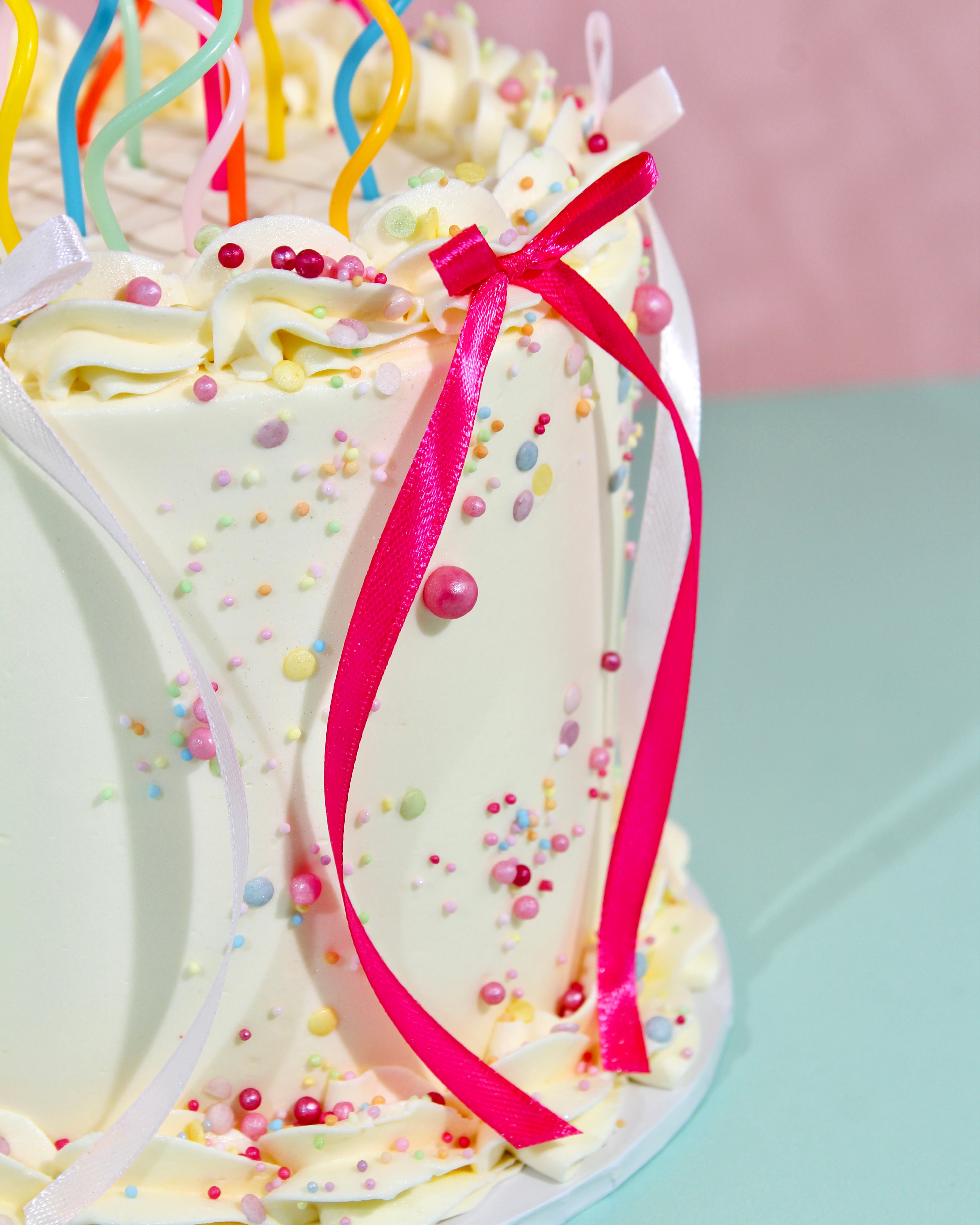 Colourful twisted birthday candles and pearl sprinkles on cream buttercream cake