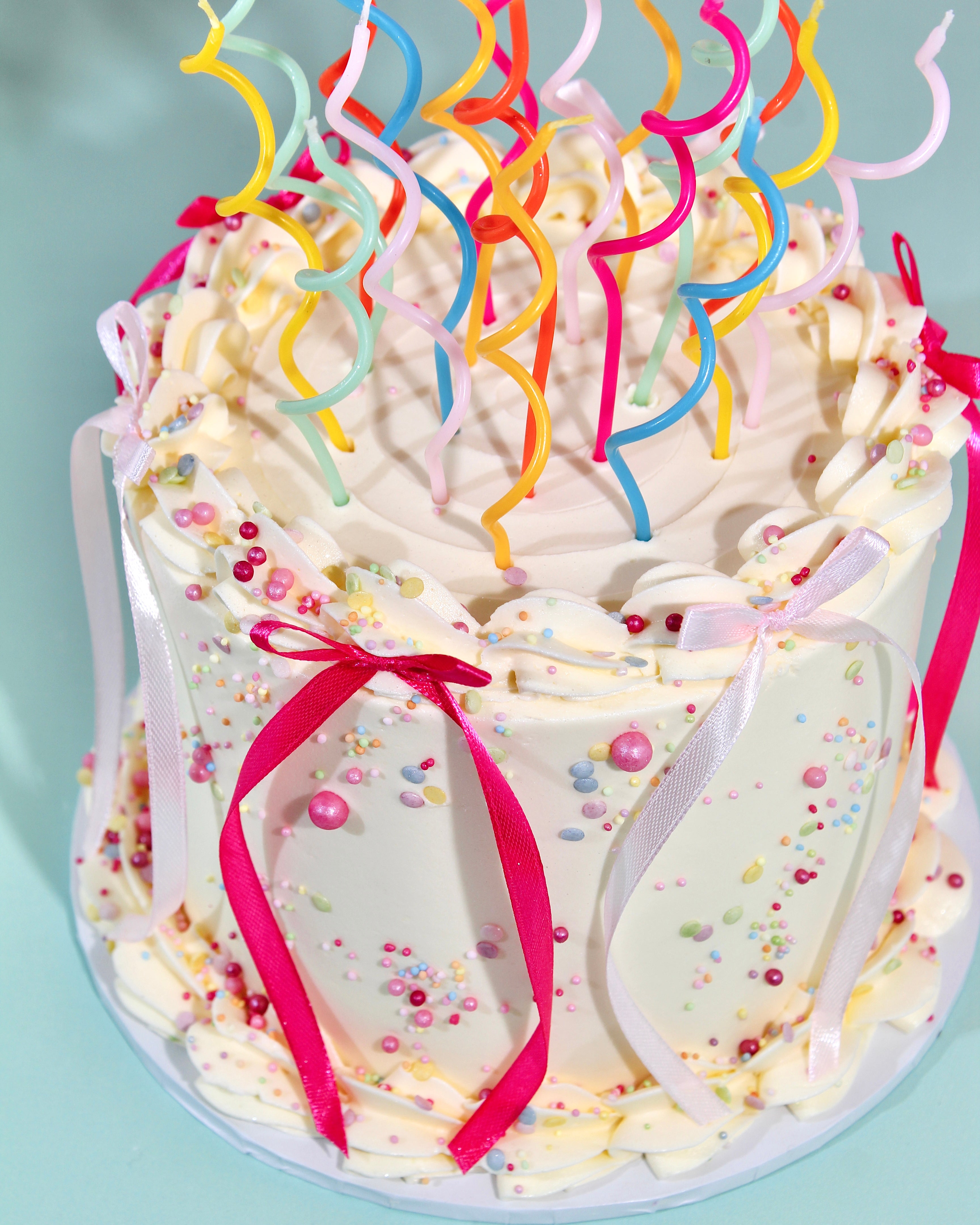 Decorative cake with colorful candles and ribbons on a light blue background