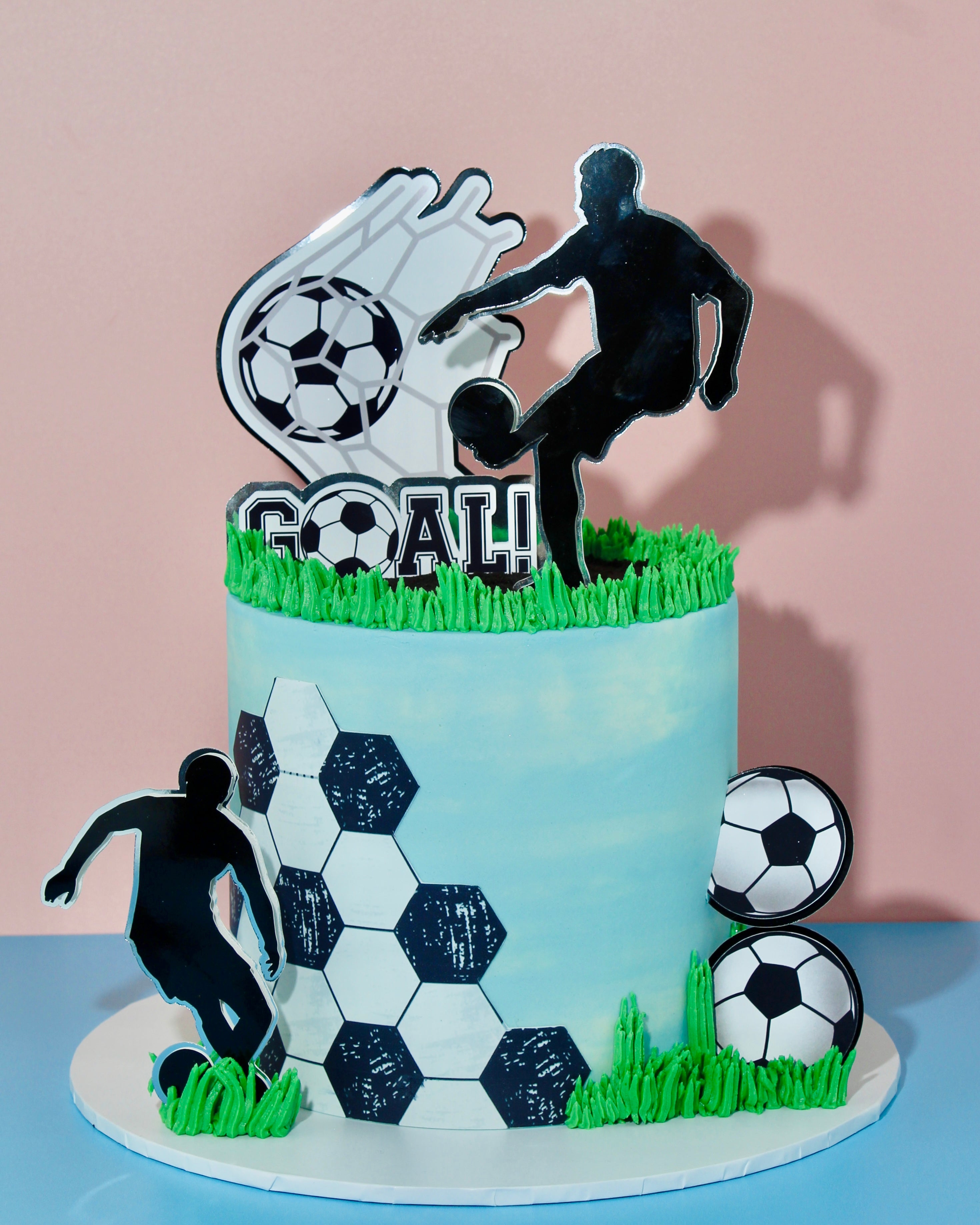 Football-themed cake with player silhouette toppers, edible grass, football decorations and hexagon football pattern