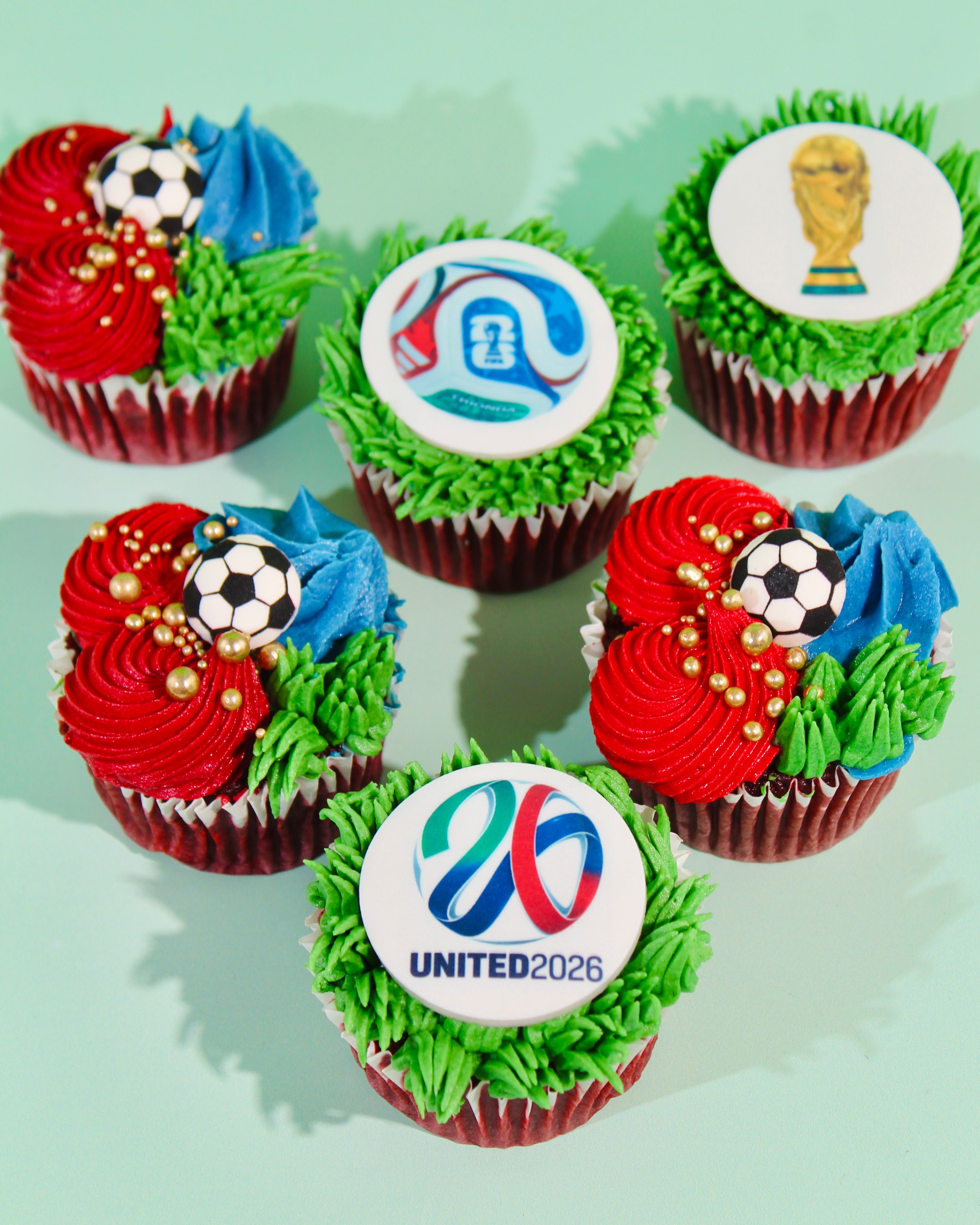 Box of World Cup 2026 cupcakes with trophy, tournament ball and football designs in red and green buttercream
