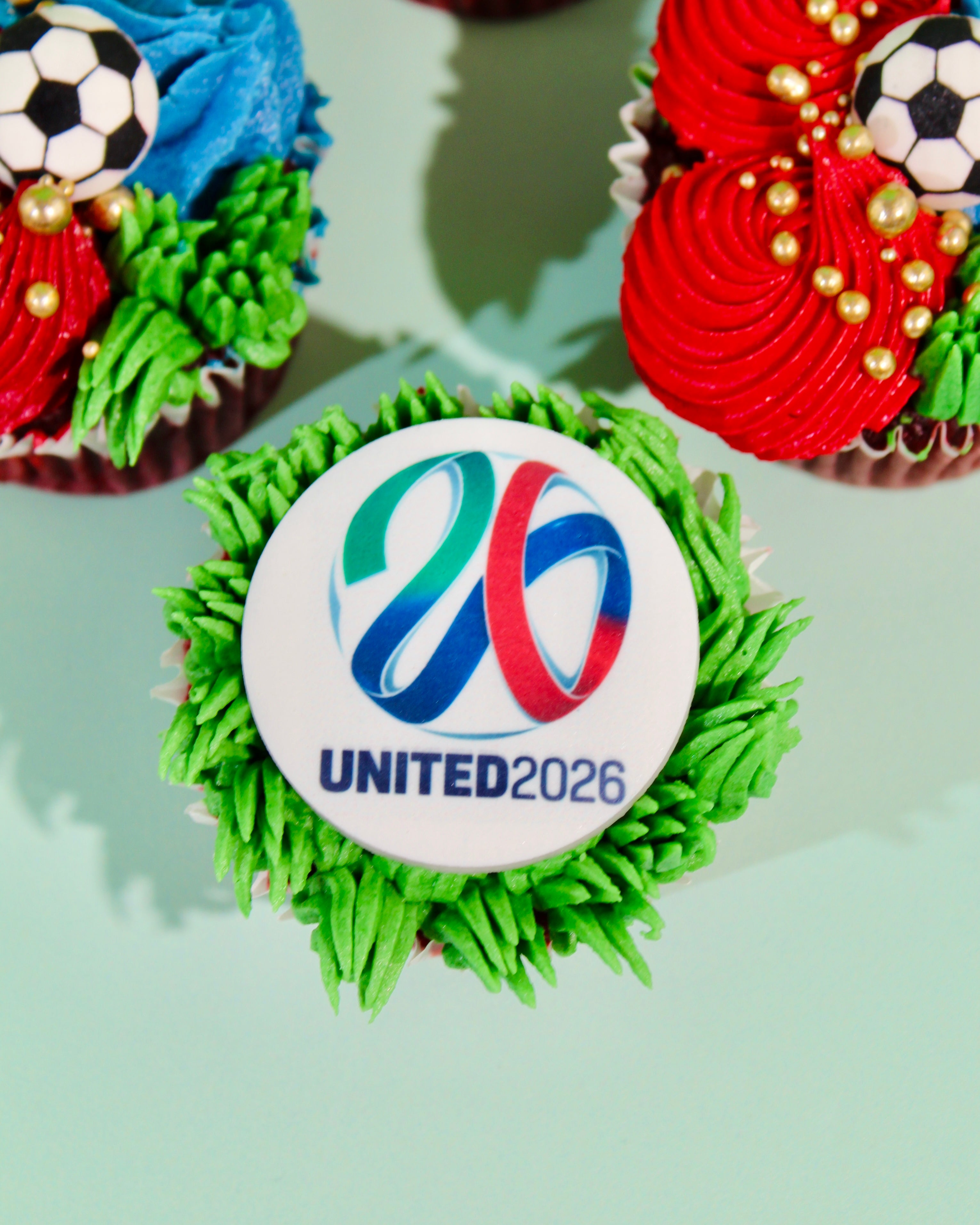 Six World Cup cupcakes showing United 2026 logo, trophy disc and football designs with gold pearl detail
